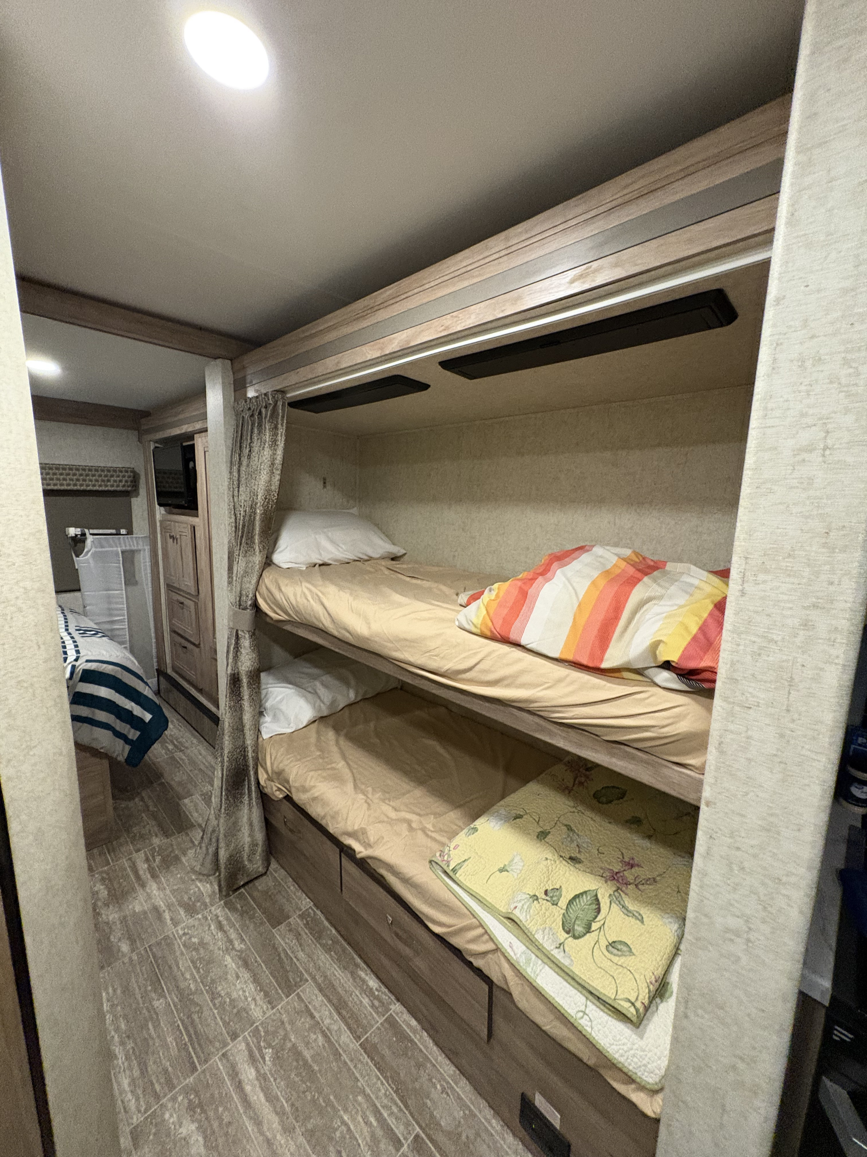Experience an RV rental: cozy bunk beds with striped and floral quilts, plus compact interior with wood-look flooring.. Forest River Sunseeker 2019