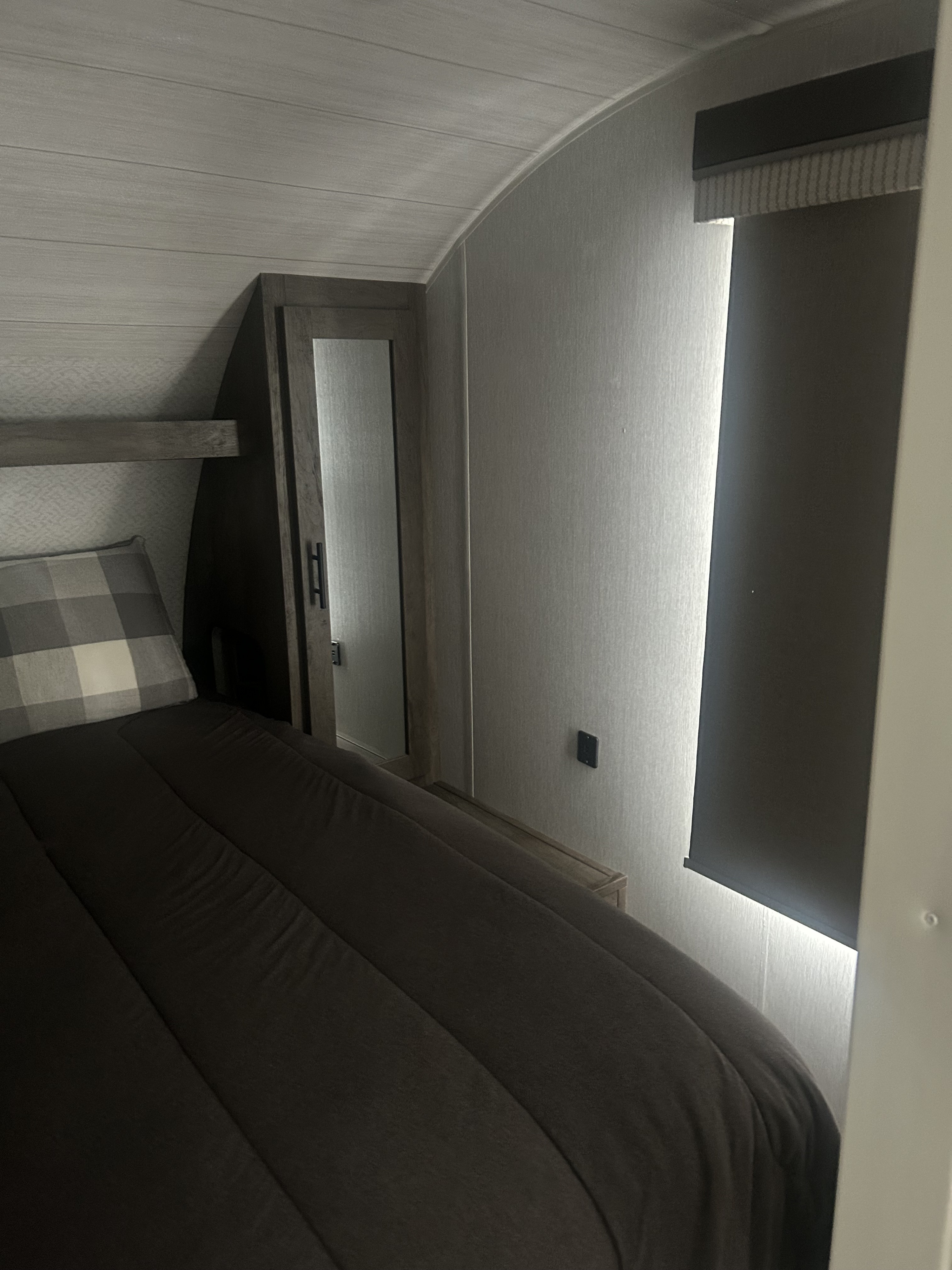 This RV rental bedroom offers a comfortable bed, mirrored cabinet, and window with blackout blind for a cozy stay.. Forest River Wildwood X-Lite 2022