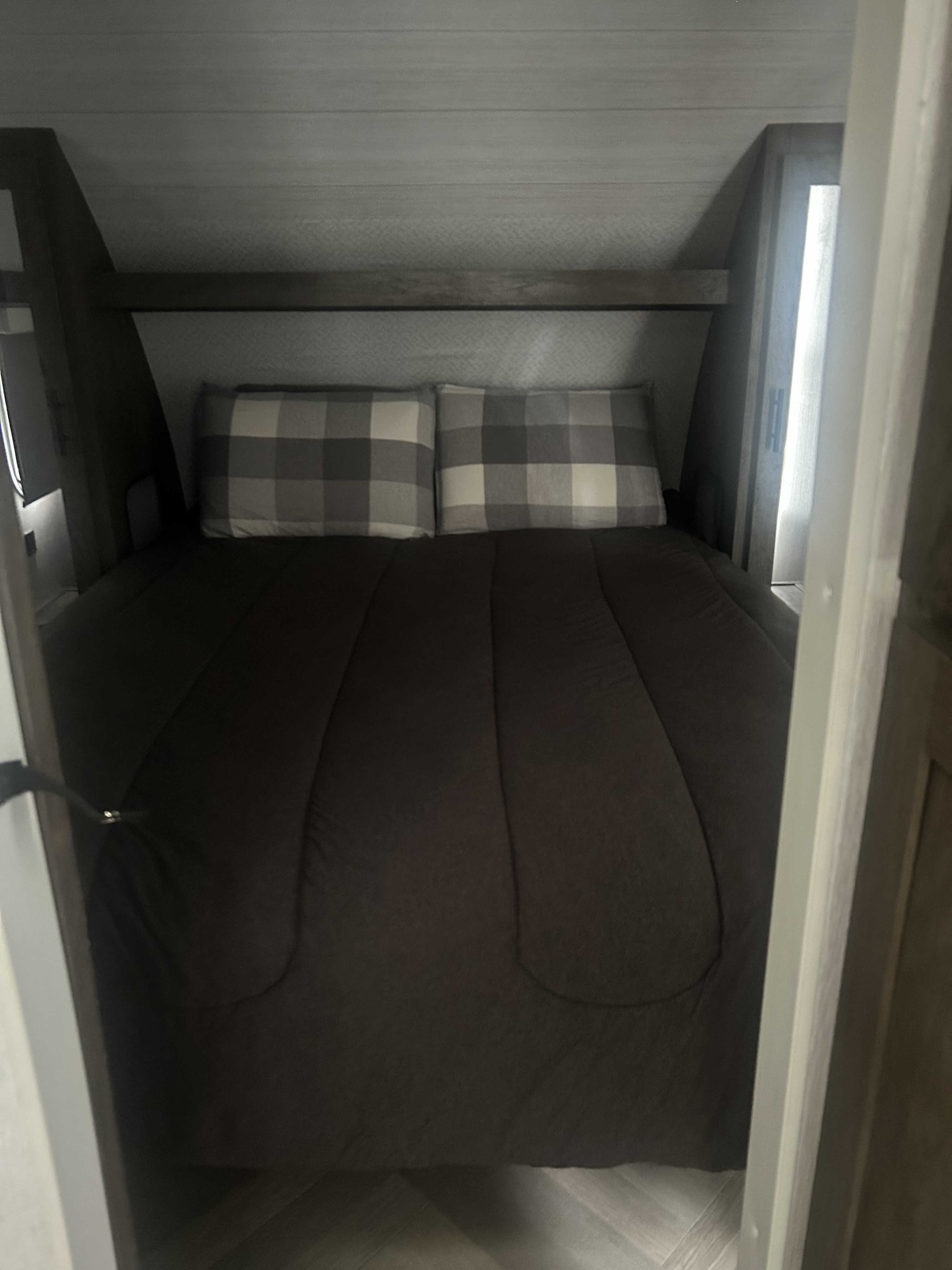 A cozy RV rental bedroom showcasing a bed with gray plaid pillows in a compact, built-in space.. Forest River Wildwood X-Lite 2022