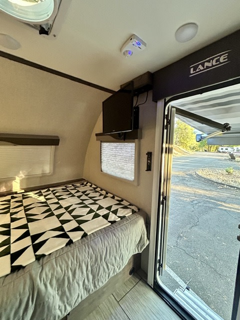 Cozy RV rental interior featuring a comfy bed, wall-mounted TV, and an open door offering a glimpse of the campsite.. Lance Manufacturing 1575 2023