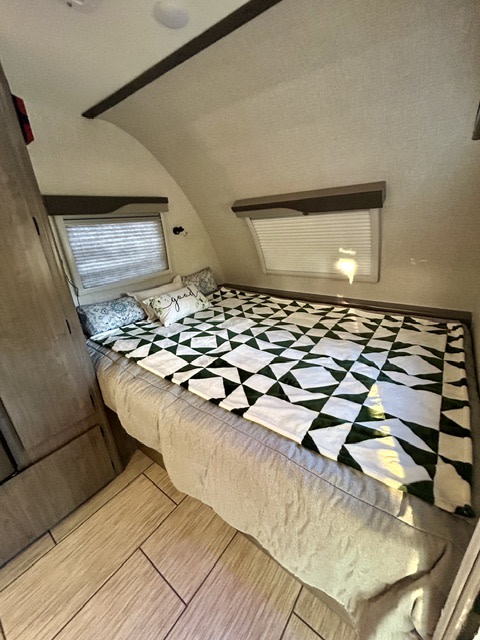 Cozy RV rental bedroom features a comfy bed with a green quilt, curved walls, and wood-look floors. Perfect for trips!. Lance Manufacturing 1575 2023