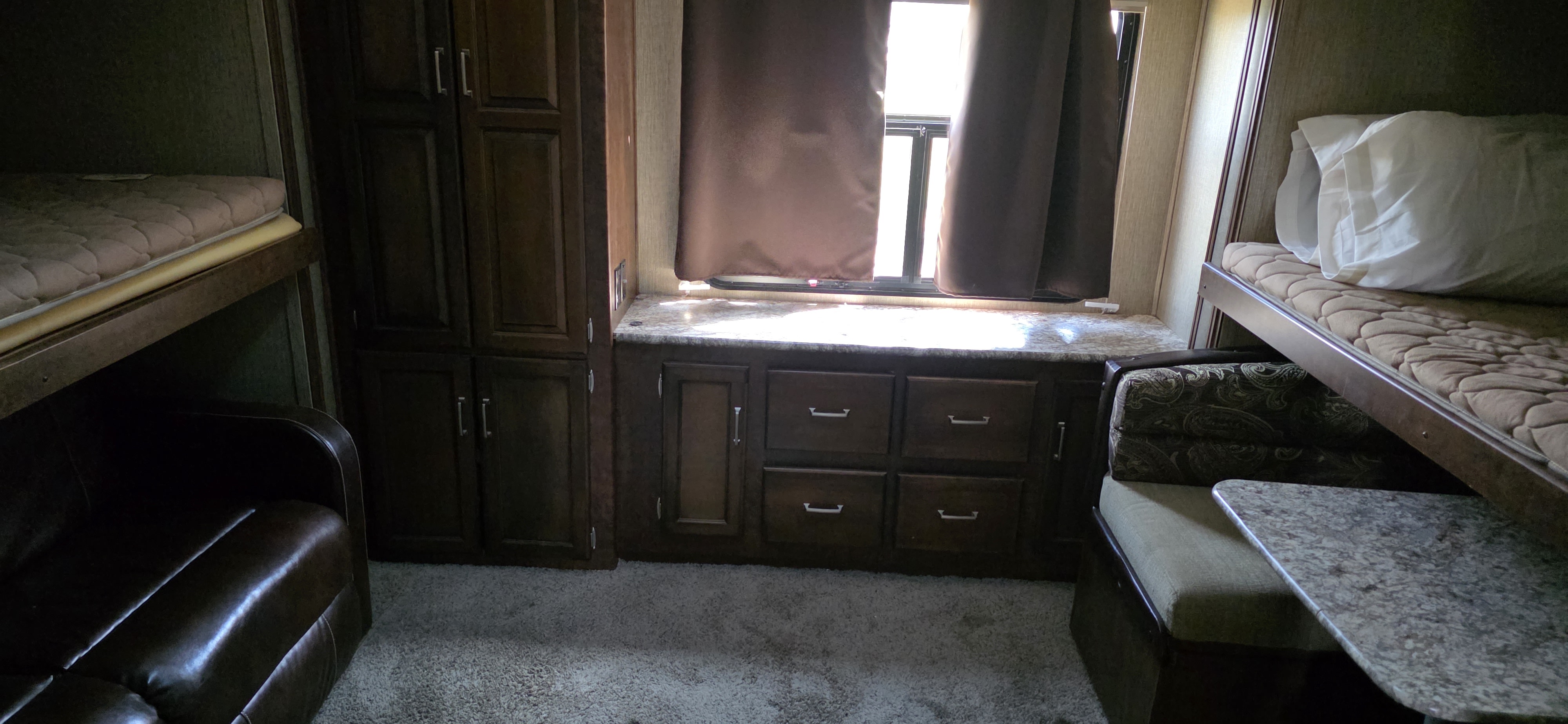 Inside an RV rental: view of a spacious living area with two sets of bunk beds, dark wood cabinets, and a dinette table.. Keystone RV Outback Super-Lite 2017