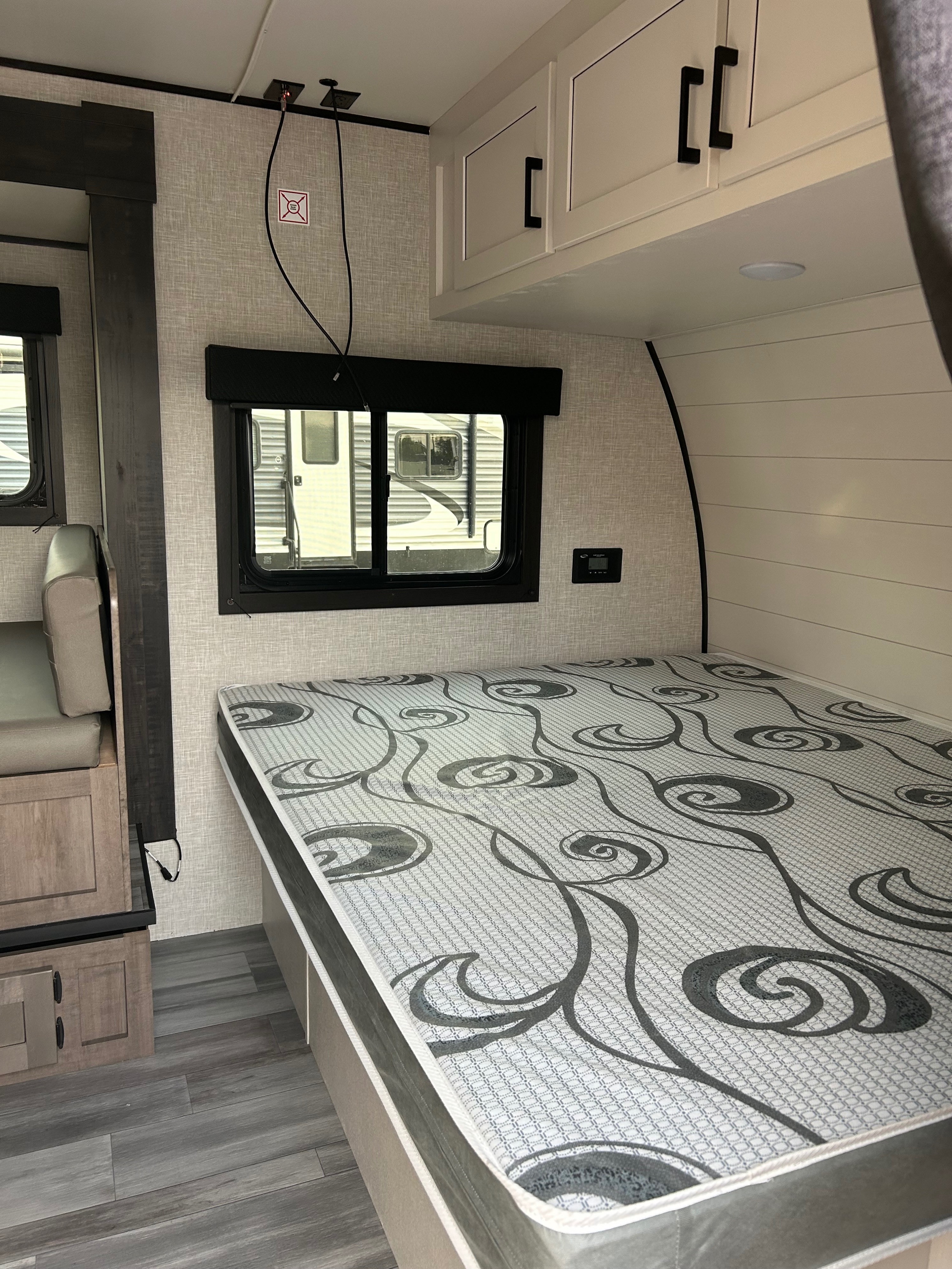 This RV rental interior features a cozy bed with patterned mattress, wood-look floor, and modern cabinetry, ideal for travel.. Open Range 180BHS 2024