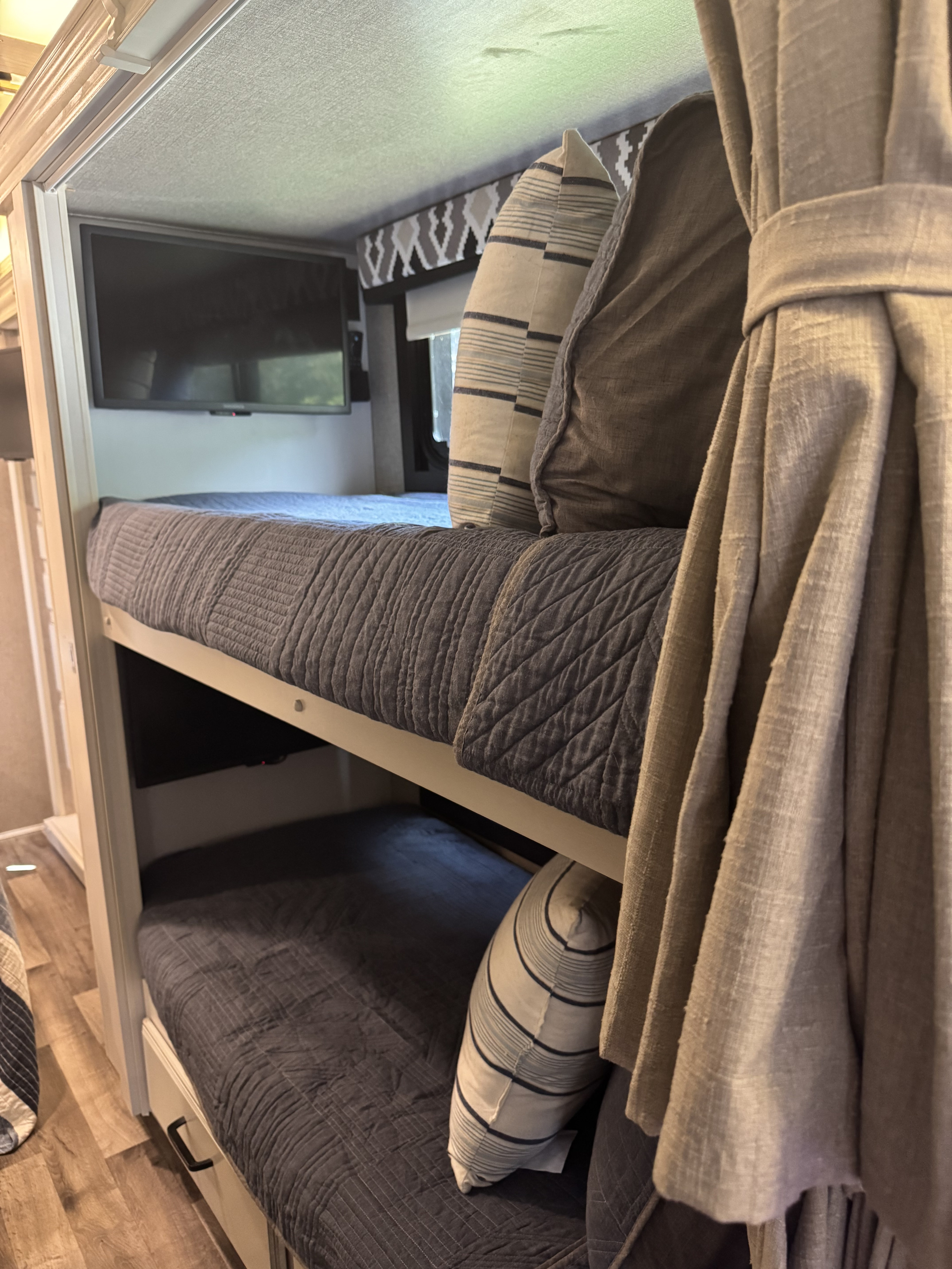 Cozy bunk beds with quilted grey bedding, striped pillows, and a mounted TV inside an RV rental.. Jayco Alante 2021