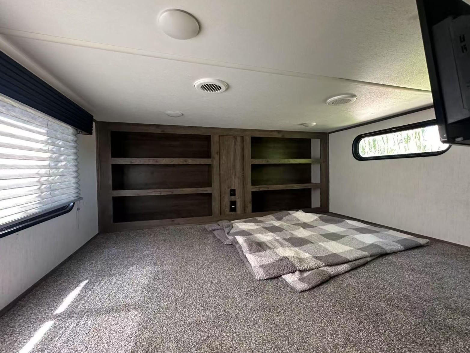 Cozy RV rental bedroom featuring carpeted platform, built-in shelves, blanket, windows, and TV.. Forest River Sabre 2021