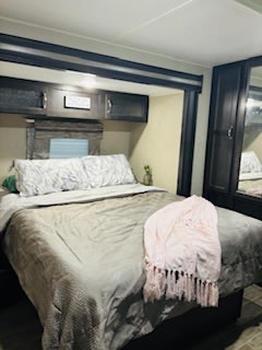 Cozy RV bedroom, perfect for your RV rental. Features a large bed, overhead storage, and a wardrobe with mirrored doors.. Forest River Palomino Puma 2019
