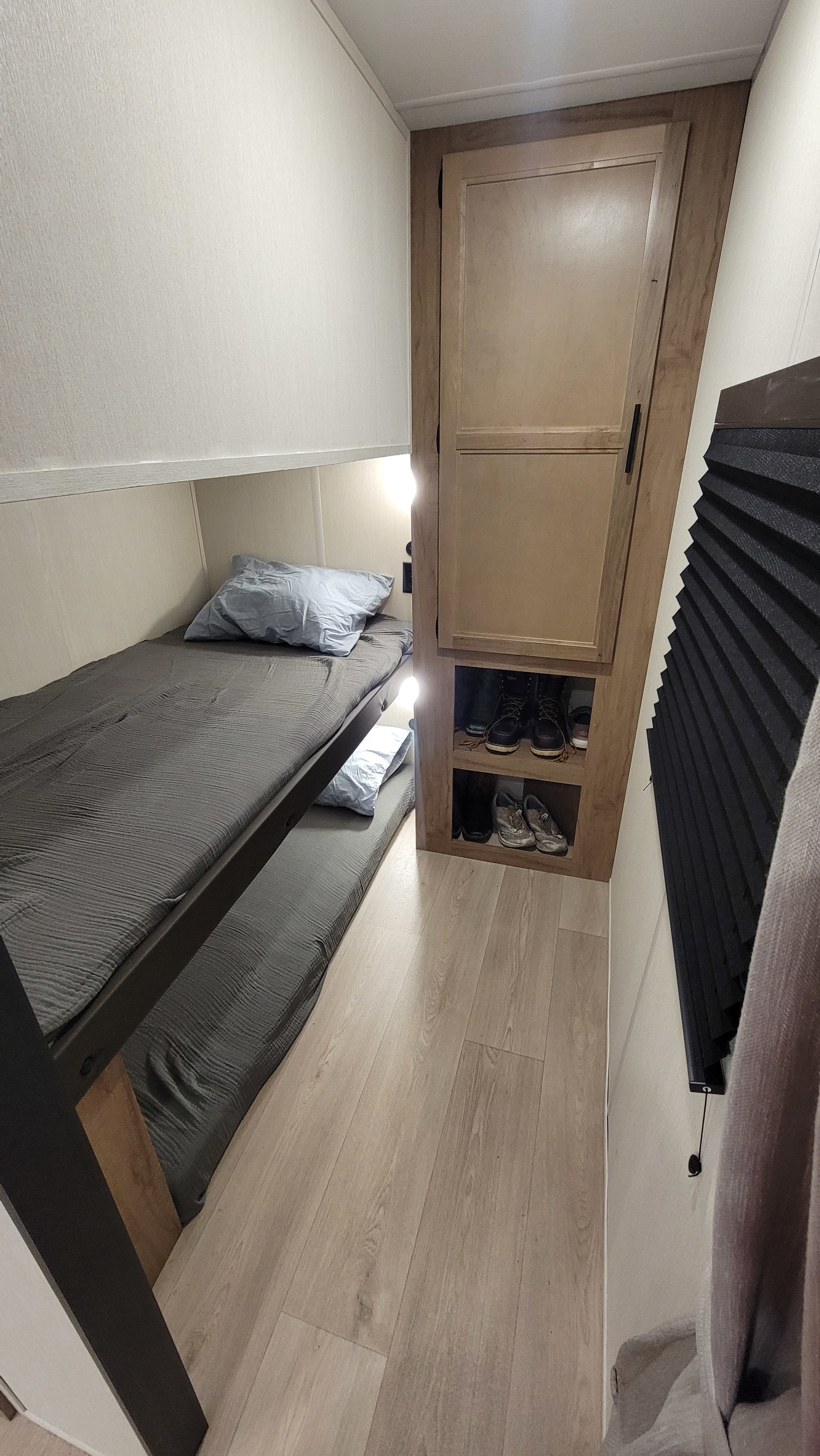 Compact RV rental interior featuring cozy bunk beds, a storage cabinet with shoes, and a pleated window shade. Ideal for travel.. Cherokee Wolf Den 294GEBG 2025