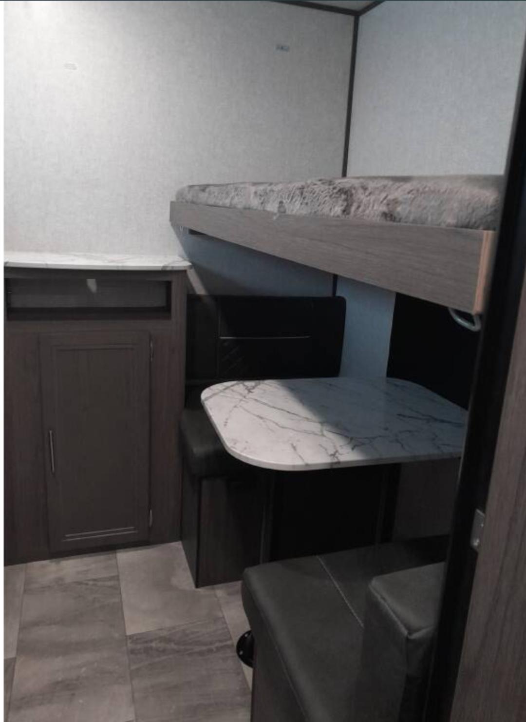 This RV rental features a cozy interior with a bunk bed above a dinette seating area and storage cabinet. Ideal for travel.. Dutchmen Kodiak Ultra Lite 2023