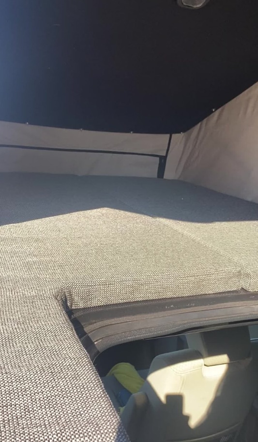 This RV rental features a cozy pop-top bed with textured grey cushions, offering a comfortable sleeping area for your travels.. honda other 2010