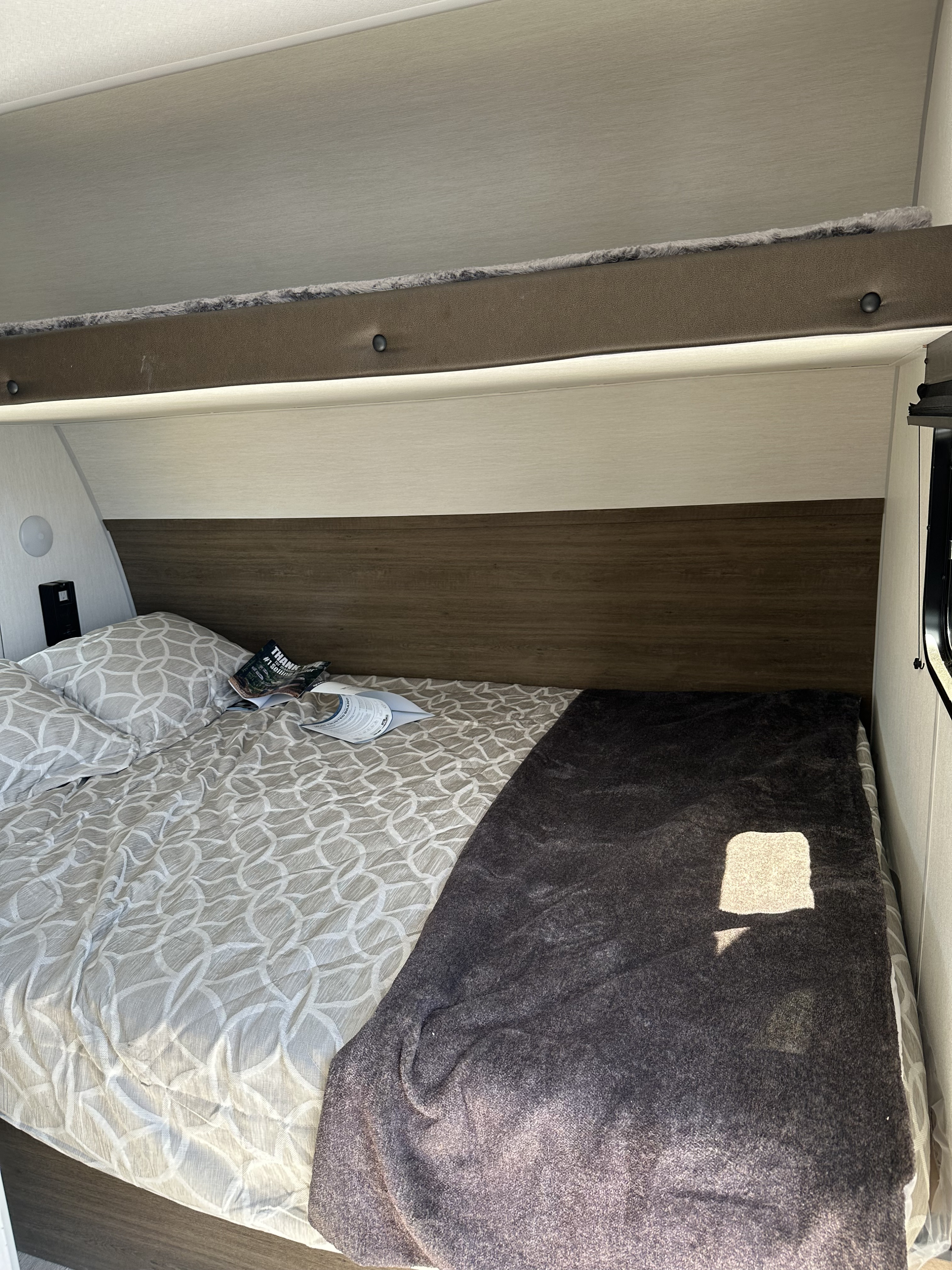 RV rental interior: cozy bedroom with a patterned bed, dark throw blanket, and overhead bunk.. Forest River Cherokee Wolf Pup 2025