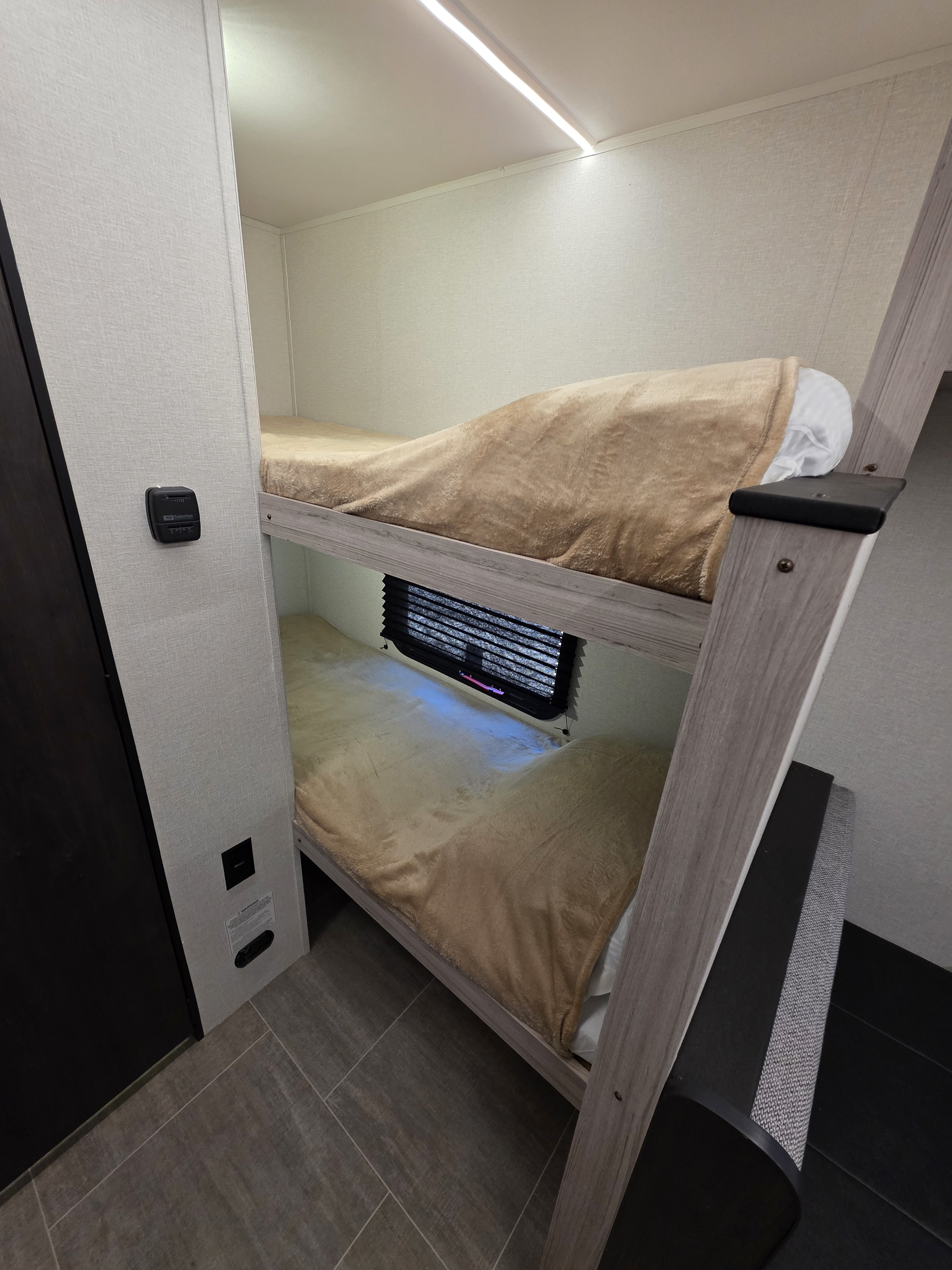 Cozy bunk beds in an RV rental, perfect for comfortable sleeping. Features soft blankets, a compact interior, and ceiling lighting.. Heartland Mallard Sport 2025