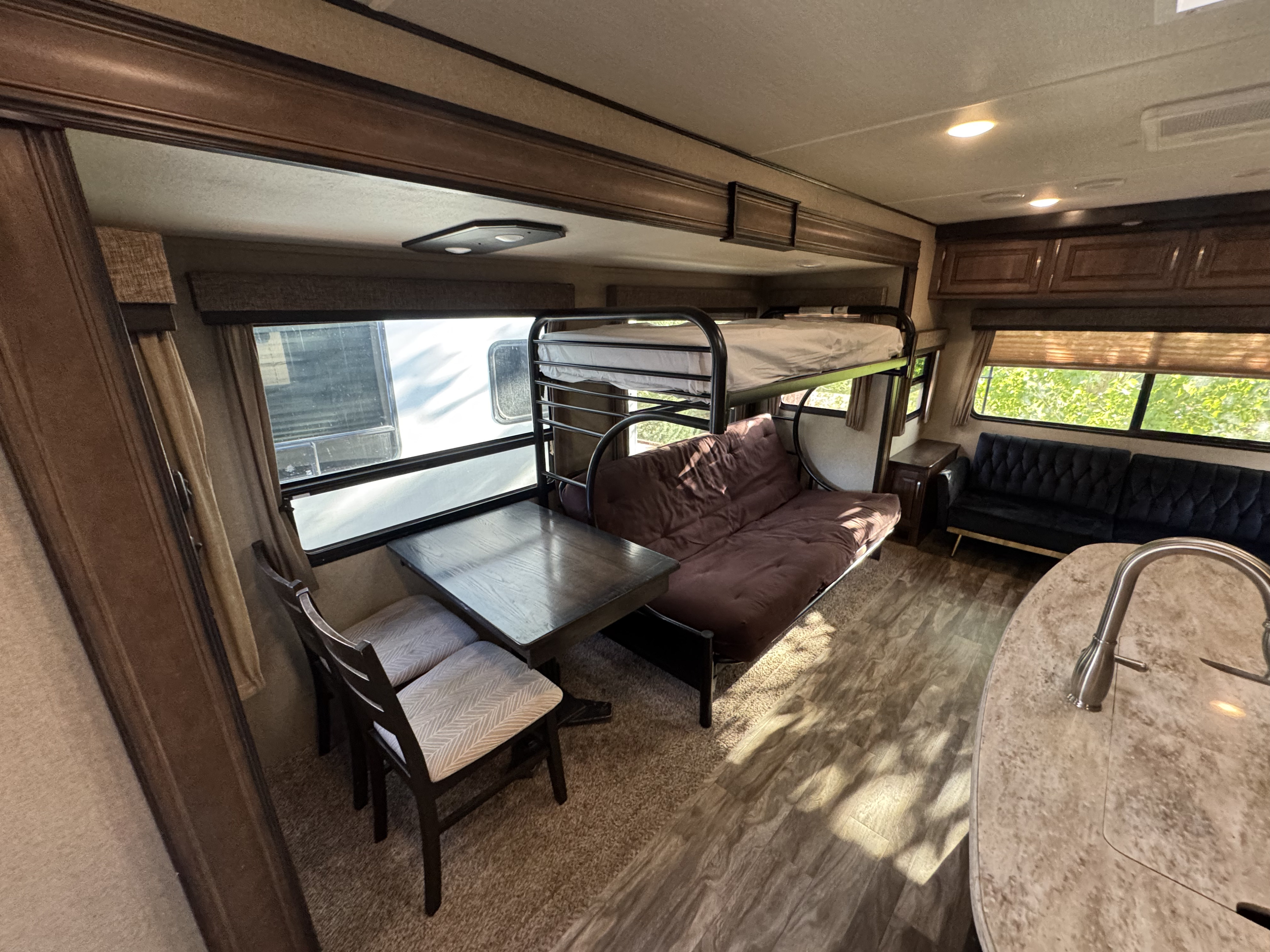 Spacious RV rental interior with bunk beds, dining area, sofa, and kitchen counter with sink, ideal for family trips.. Grand Design Reflection 2018