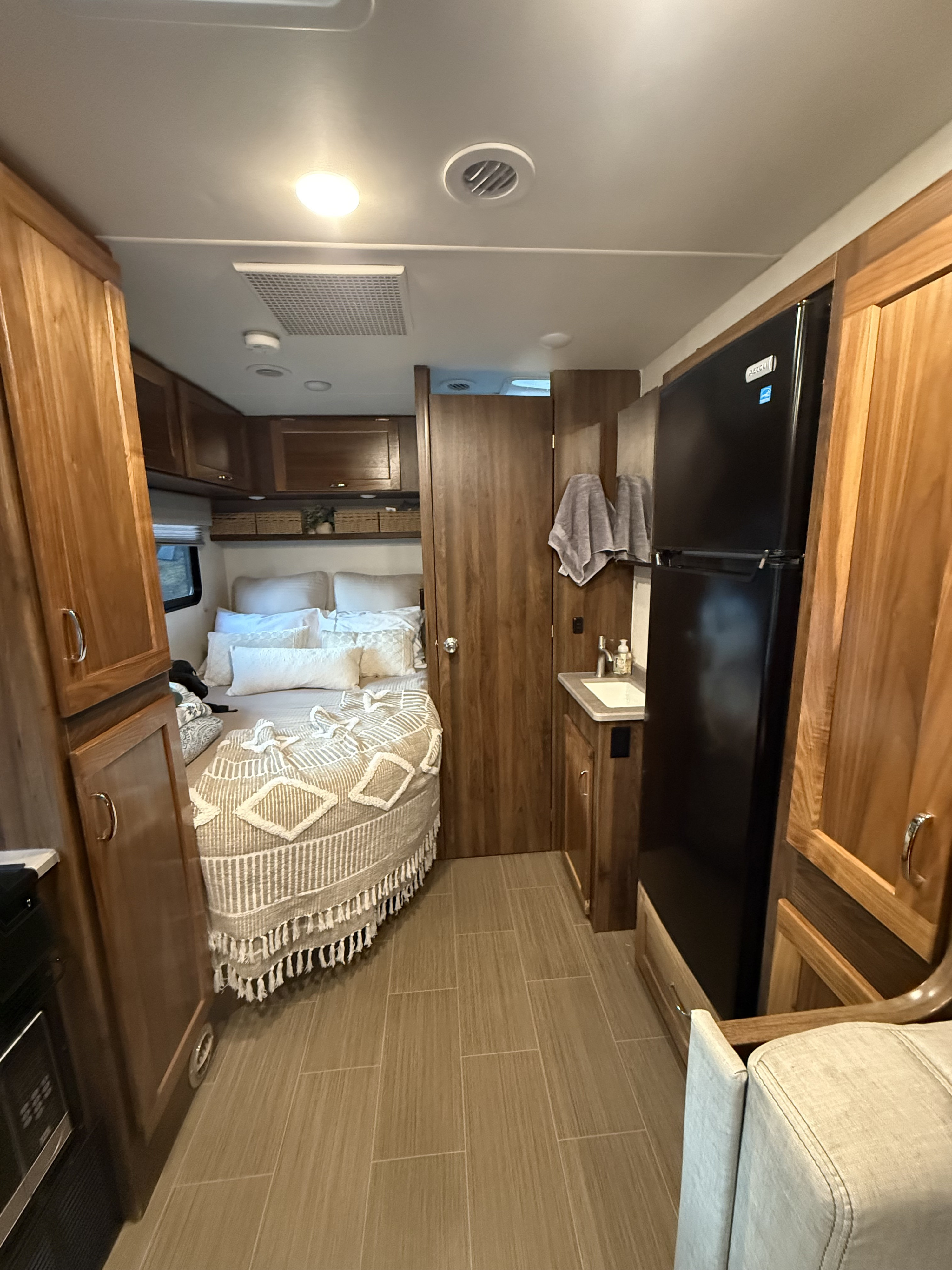 This rv rental features a cozy bedroom with a patterned blanket and compact kitchen area with sink and fridge.. Winnebago Vita 2020