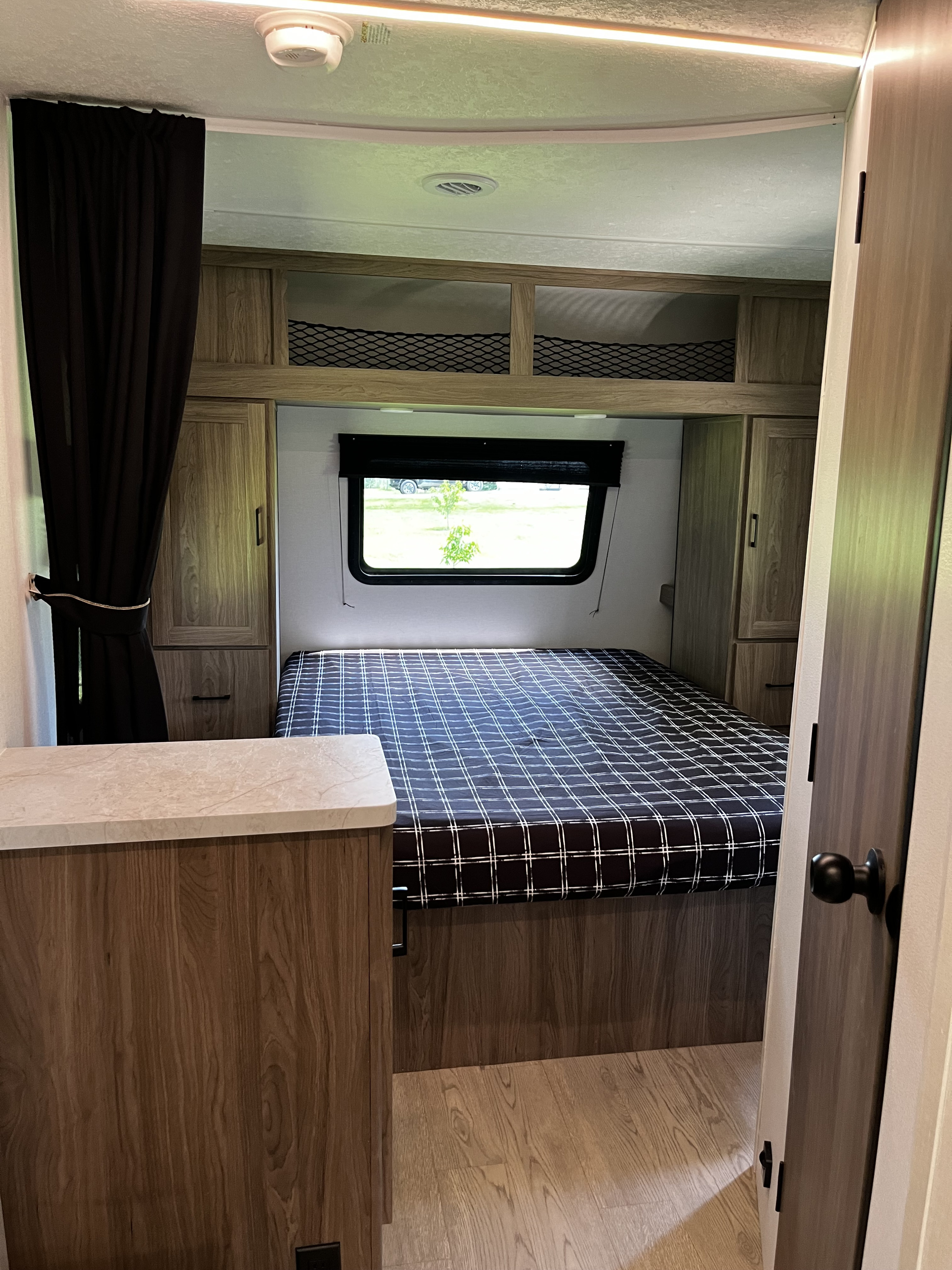 View of a modern RV rental bedroom from the doorway, featuring a plaid bed, wood cabinets & natural light.. Coachmen Freedom Express 247se 2025