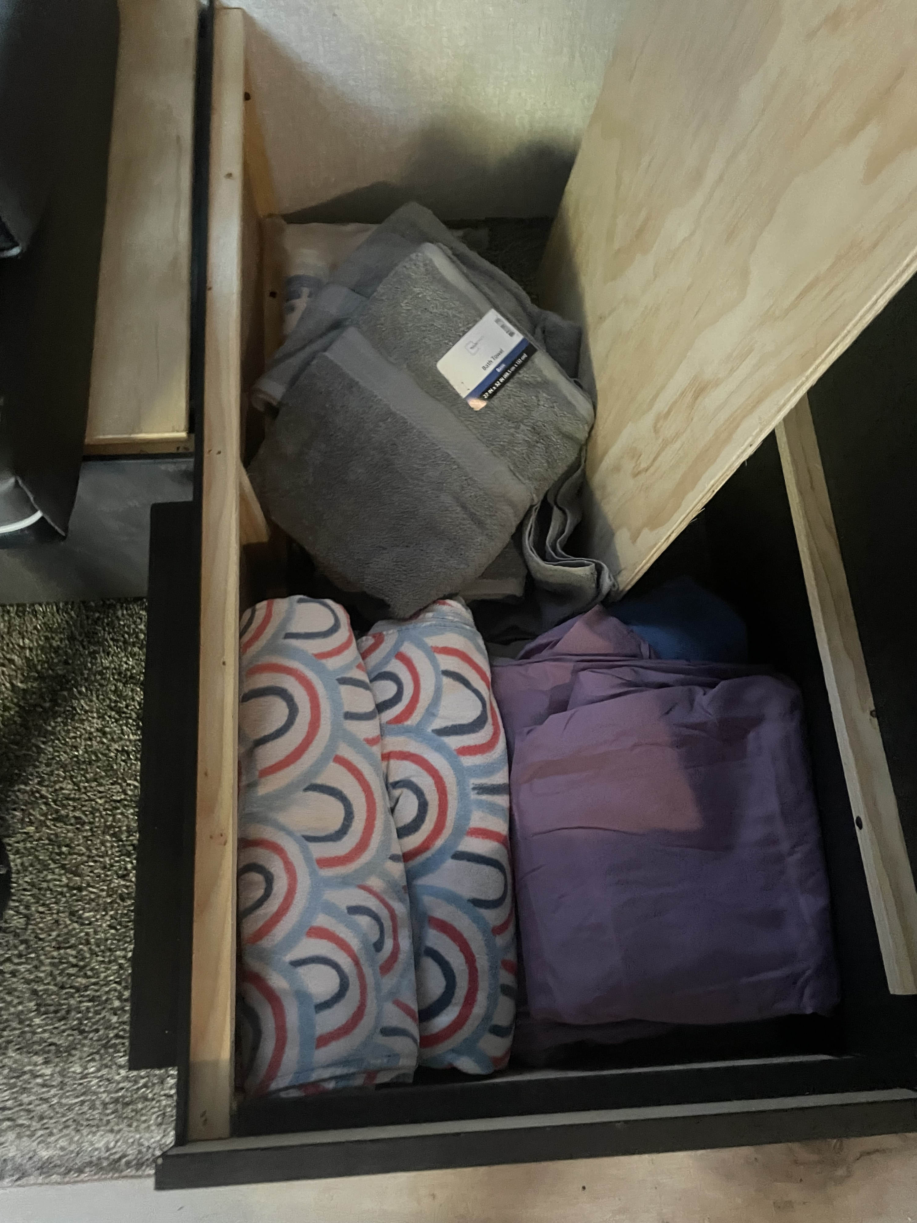 RV rental storage compartment with neatly folded gray towels, two rolled patterned blankets, and purple bedding.. KZ sportsman bh281 2022
