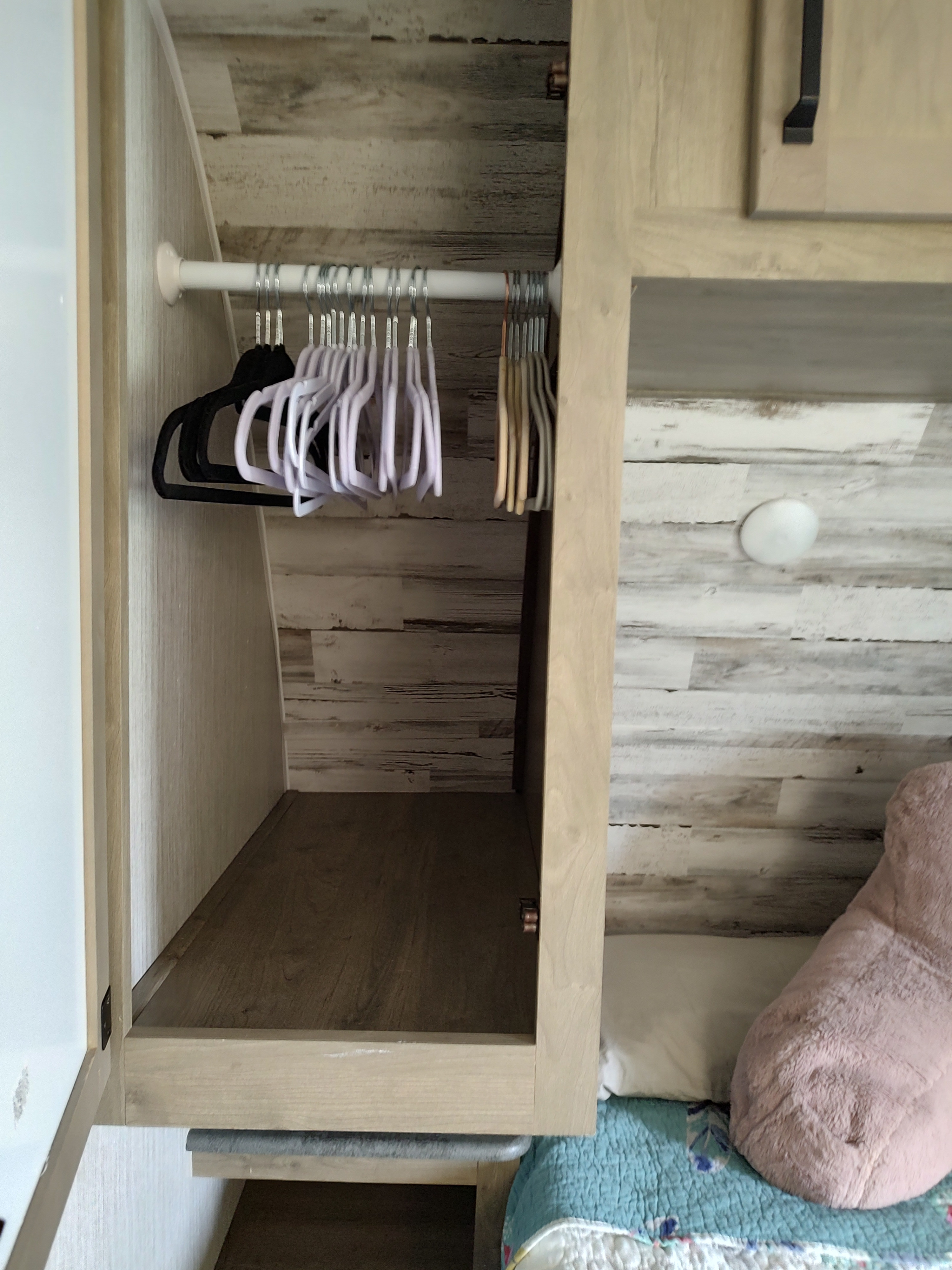 RV rental interior: a compact bedroom closet with hangers and shelf, next to a bed with a white pillow and pink fluffy pillow.. Palomino Puma 26RLS 2022