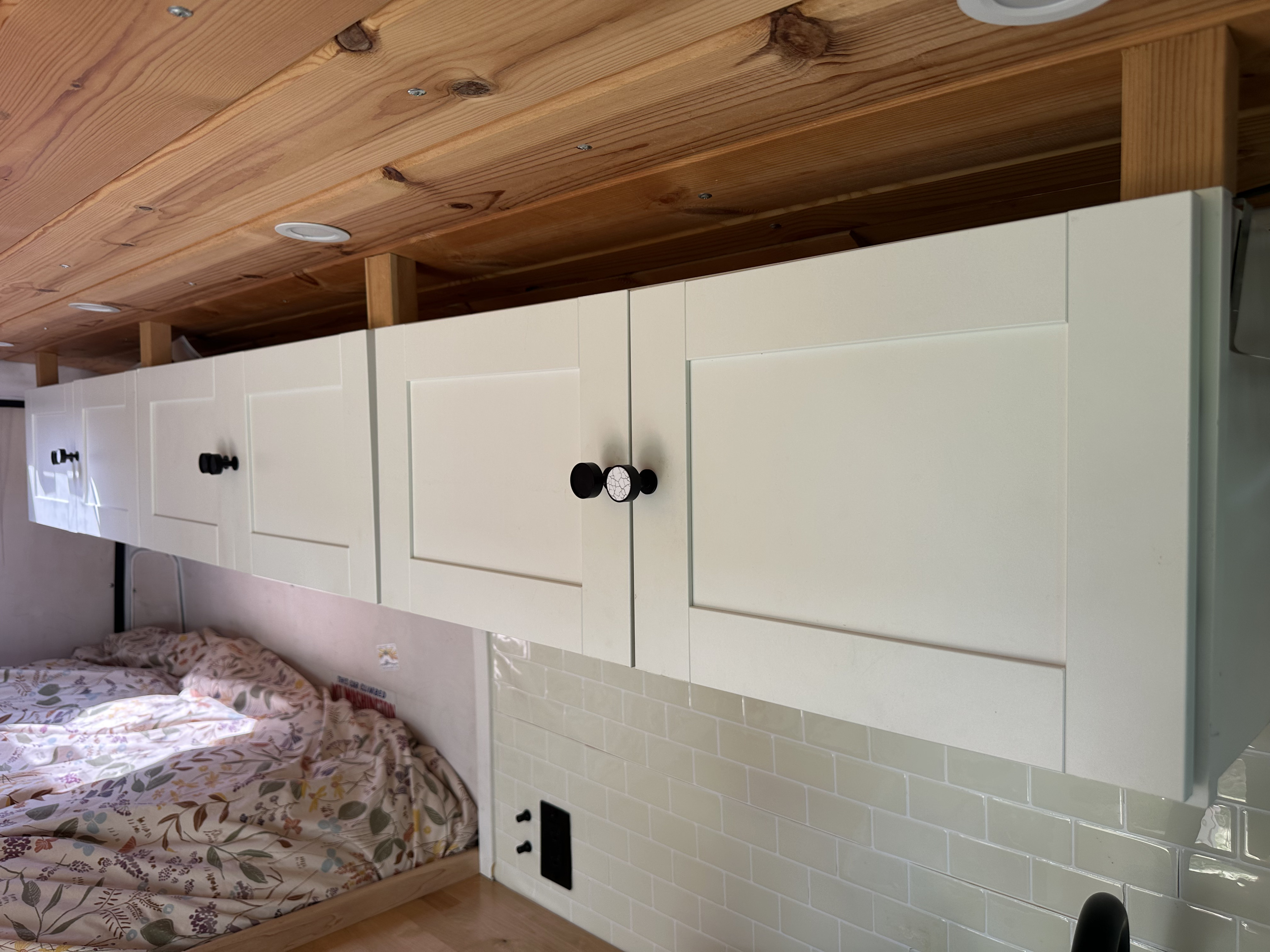 Cozy RV rental interior featuring light overhead cabinets, a warm wooden ceiling, and a comfortable bed area.. Dodge B Van 2018