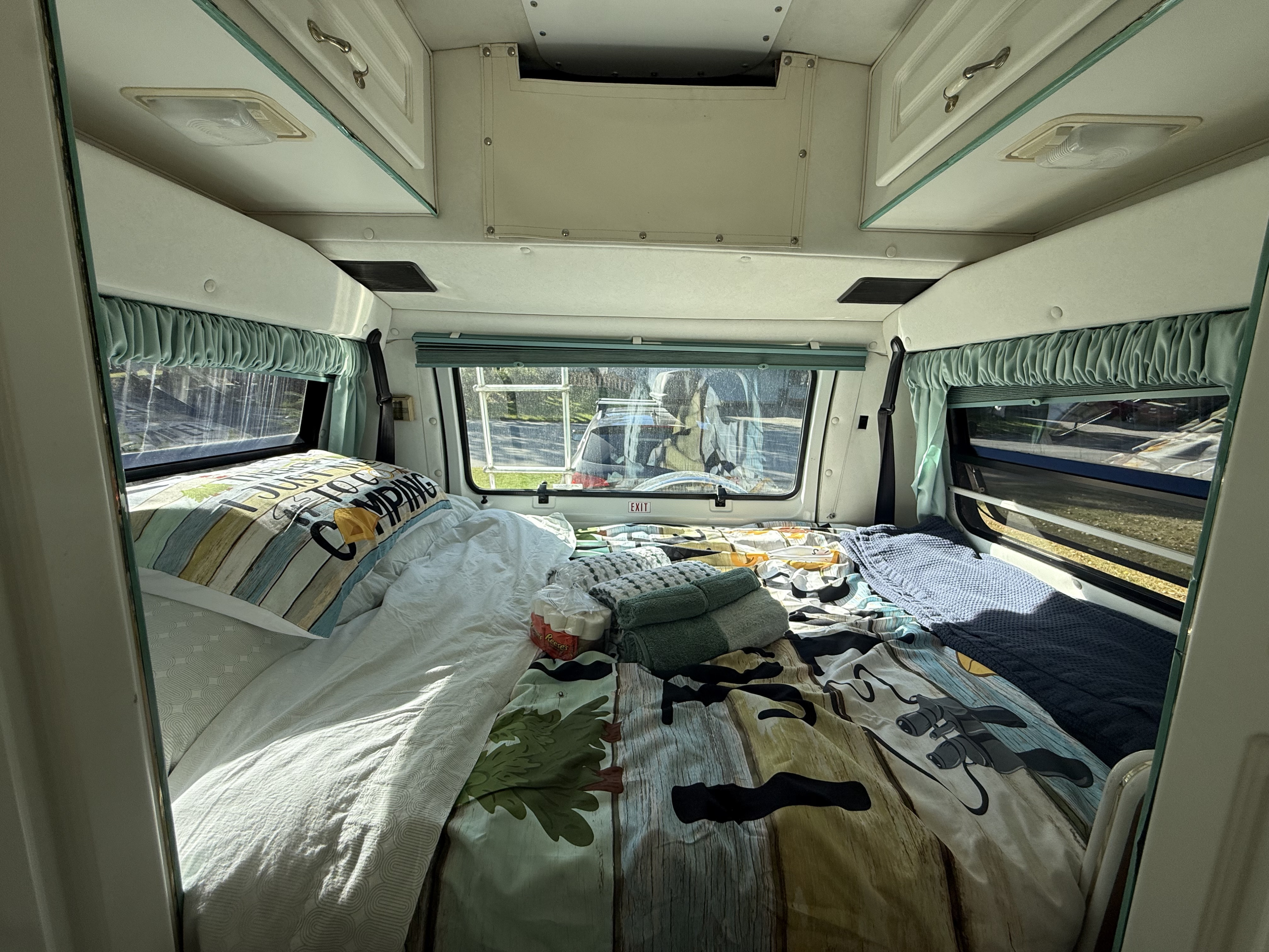 Full-Size Bed with Memory Foam Topper – Sleeps two adults comfortably after a day of exploring. Bed with camping comforter, pillows, windows with curtains, and overhead storage.. Pleasure Way Freedom 1995