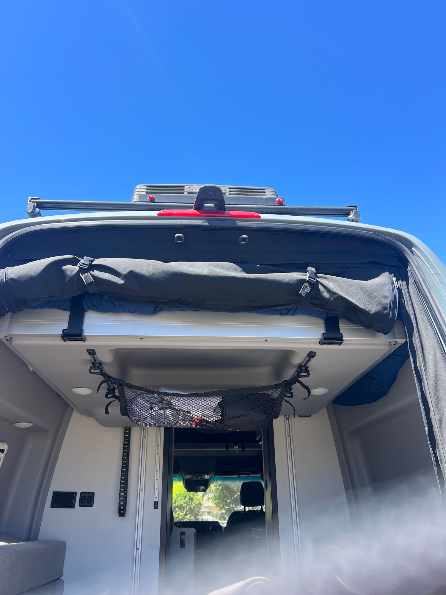 Inside an RV rental: open rear hatch shows overhead bed/storage area, roof rack, and a hanging mesh net. Perfect camper van setup.. Winnebago Revel 2022