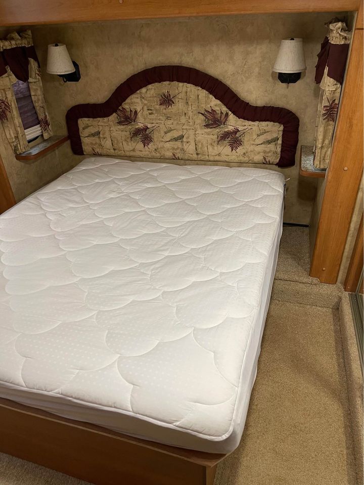 Cozy RV rental bedroom featuring a clean white mattress, decorative headboard, and two wall-mounted lamps. Ideal for your travels.. Keystone RV Montana 2007