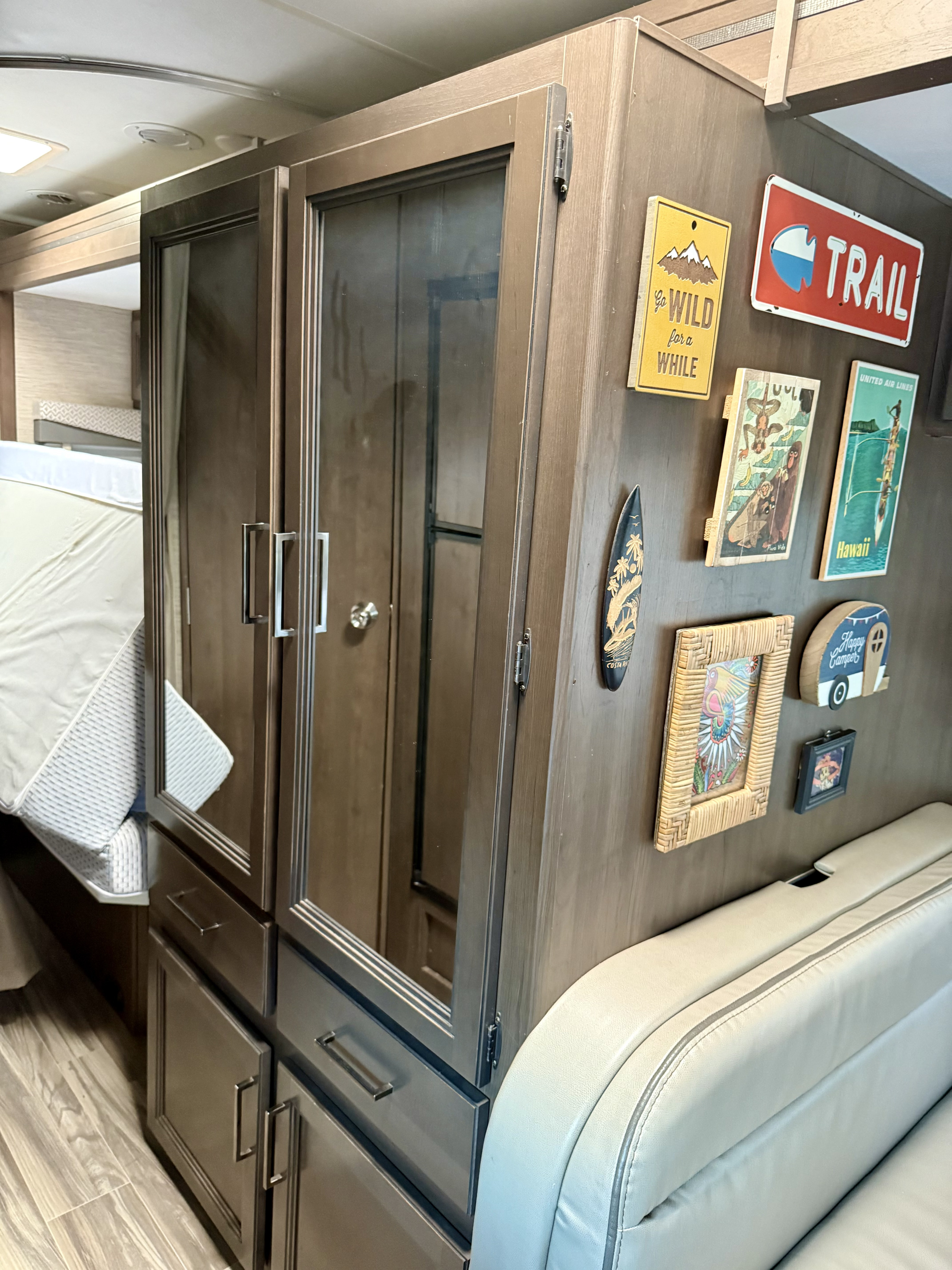 RV rental interior featuring a tall cabinet, cozy sofa, and travel-themed decor. A tilted mattress shows smart space utilization.. Thor Four Winds 2022
