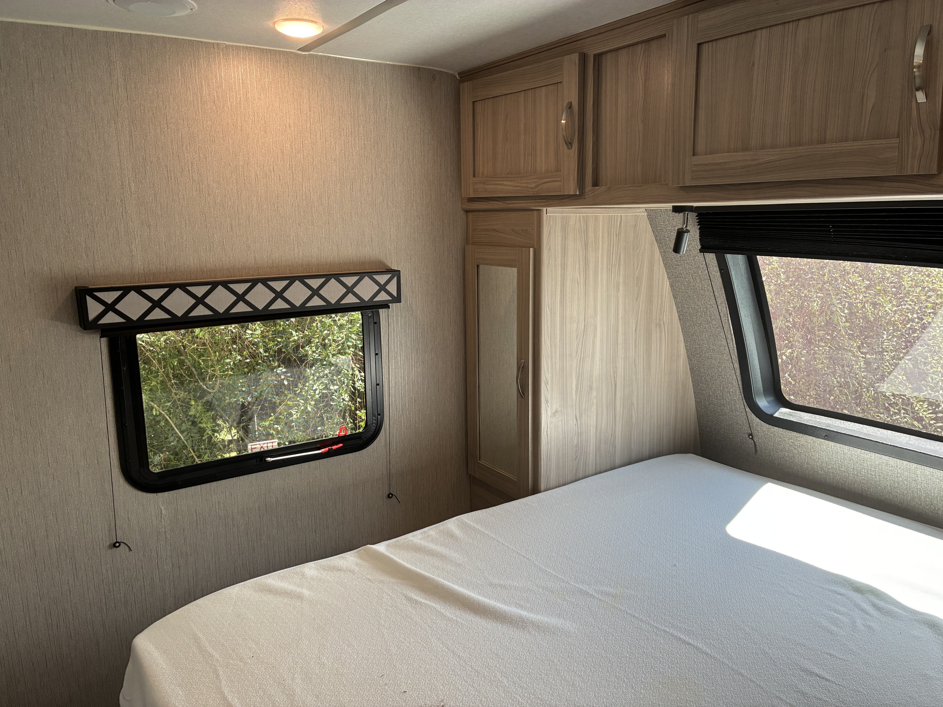 Step into this RV rental bedroom: featuring a white bed, window with nature views and an exit sign, plus wooden storage cabinets.. Coachmen Freedom Express 2021