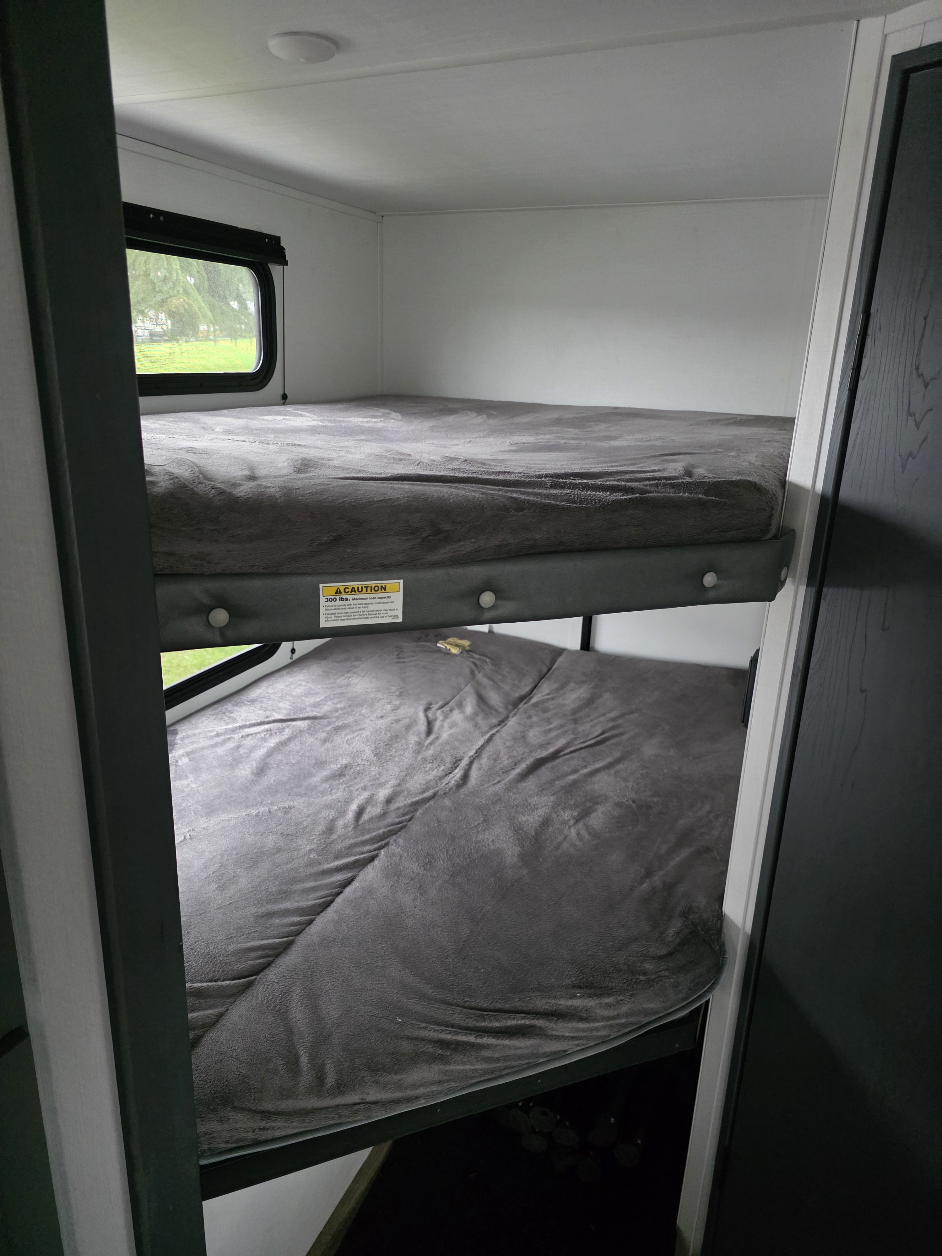 Cozy RV rental bunk beds with gray bedding and a window view, ready for your next travel adventure.. Keystone RV Bullet Crossfire 2024
