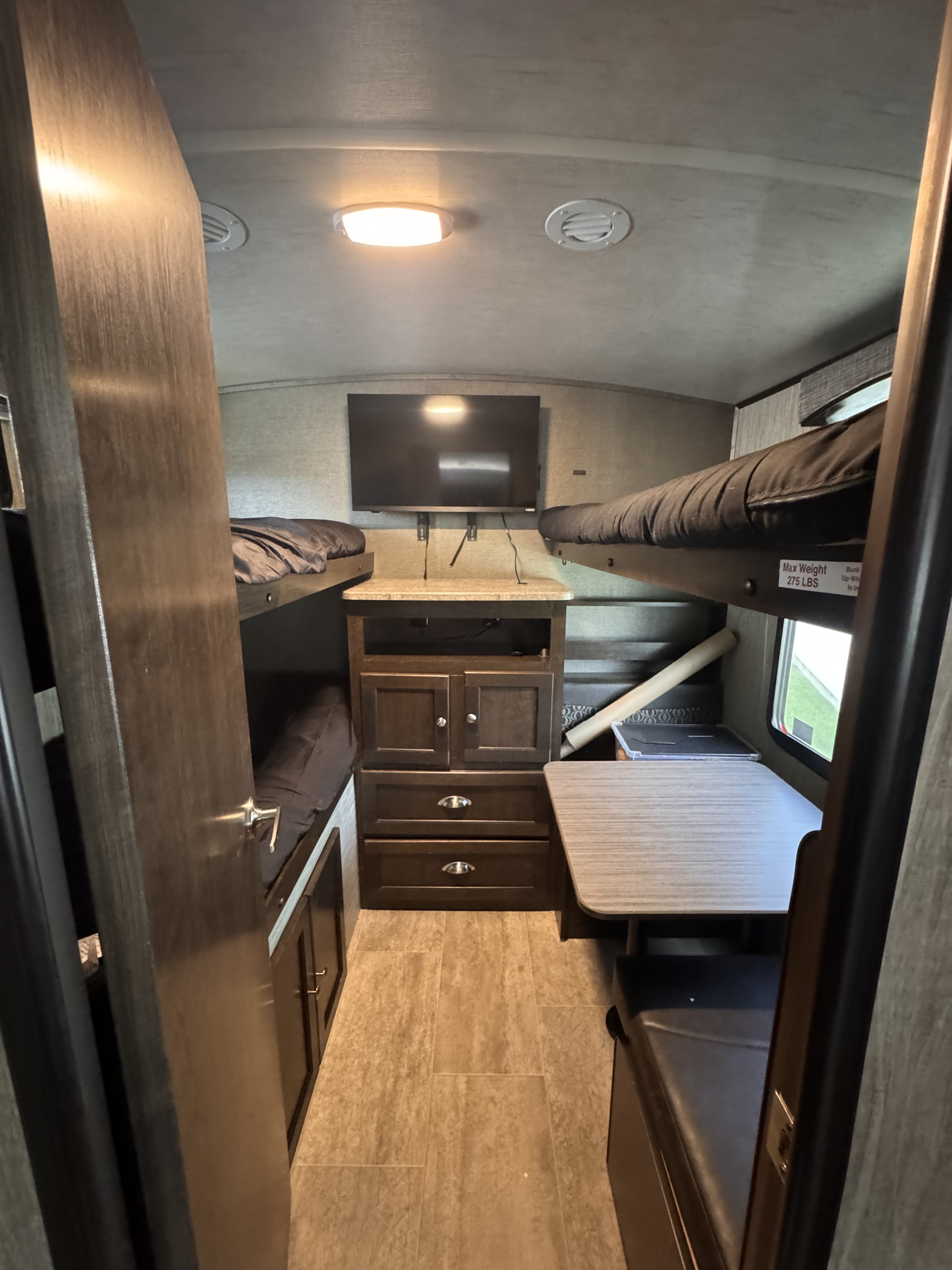Inside this RV rental: Bunk beds, a mounted TV, storage, and a dinette create a compact living space with tiled floor.. Heartland RVs Sundance 2019