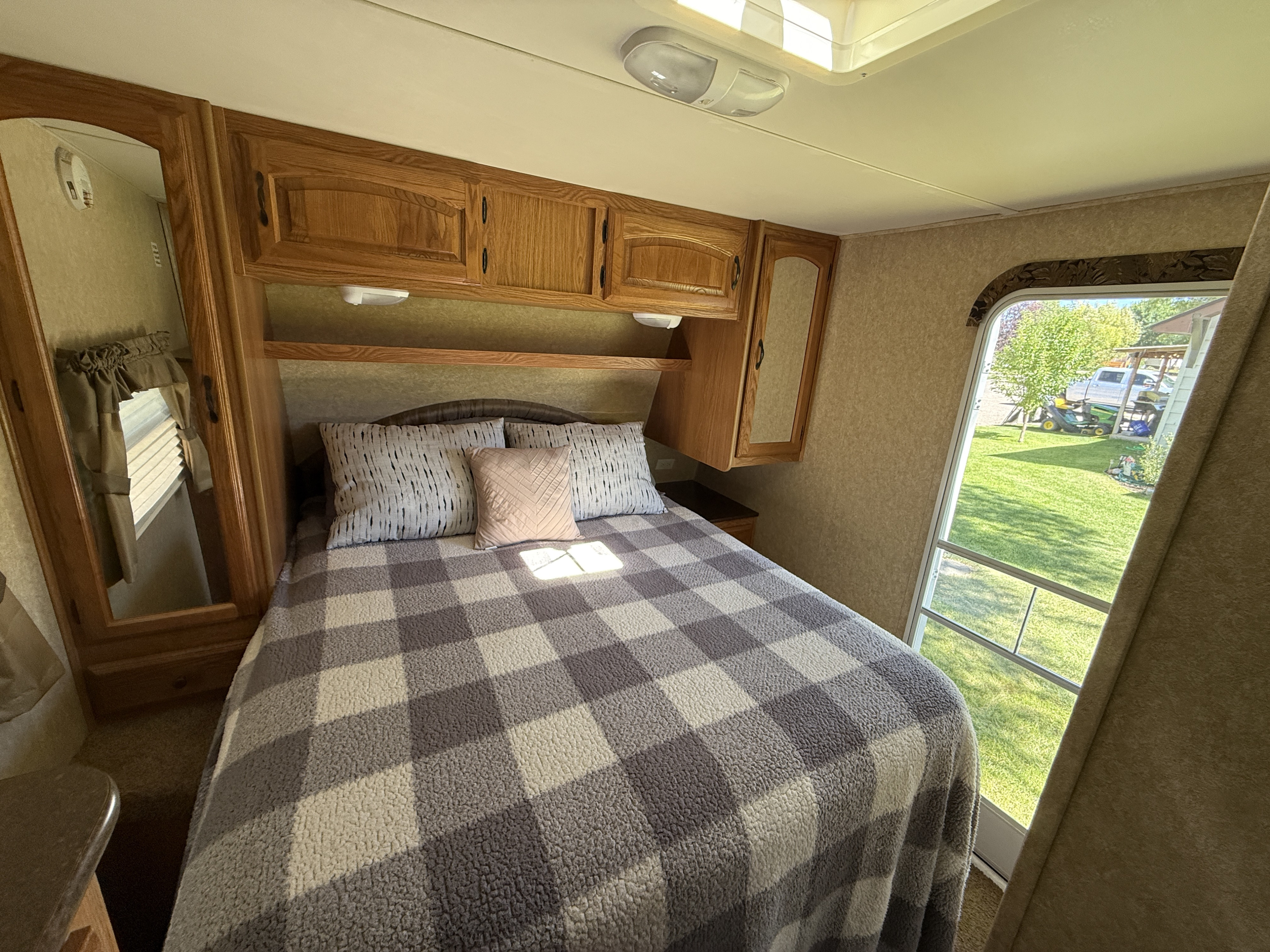 Cozy RV rental bedroom featuring a comfy bed, wooden cabinetry, and a bright window view of the scenic outdoors.. Denali Denali Trailer 2011