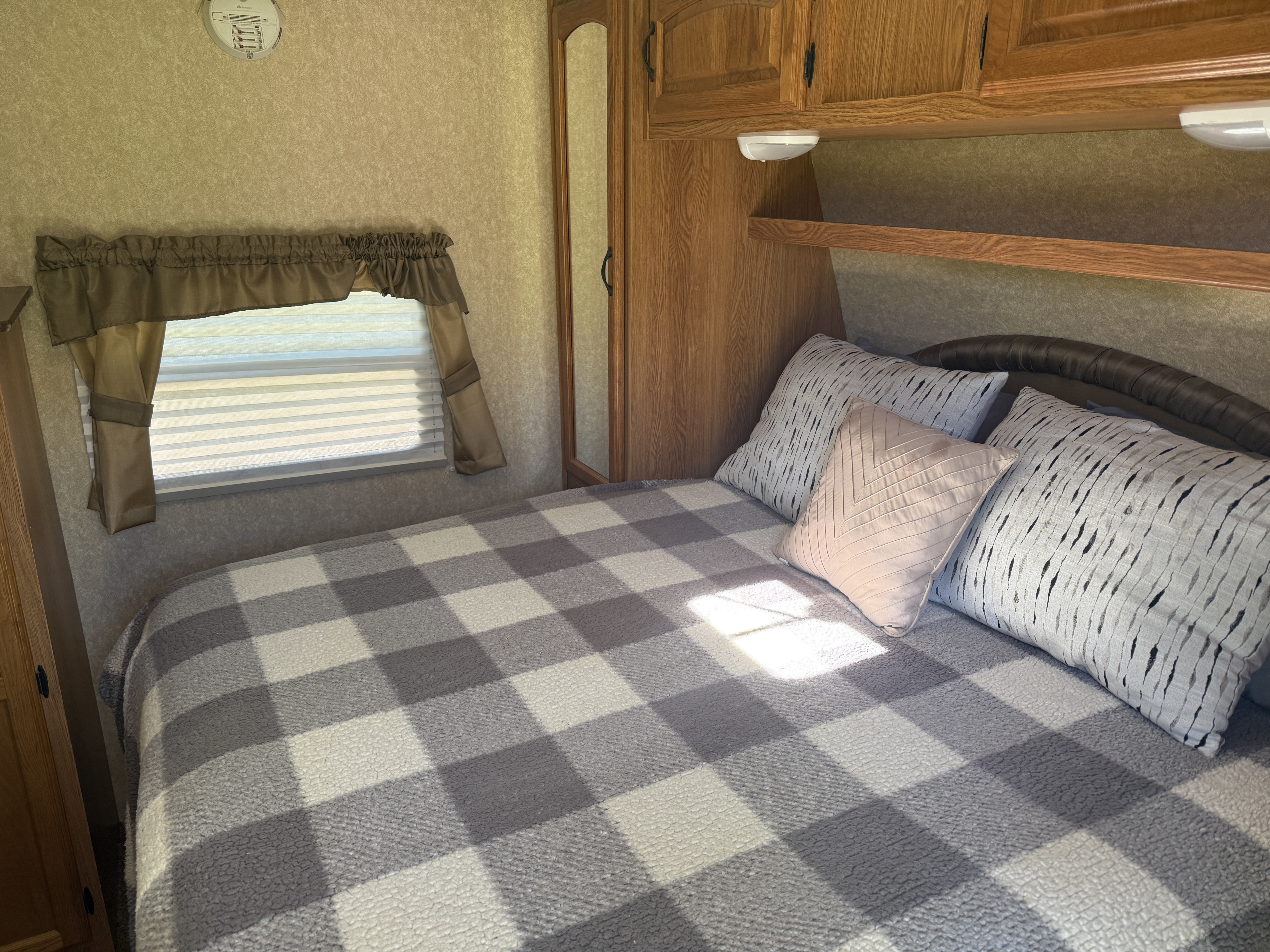 Cozy RV rental bedroom featuring a comfortable bed with plaid blanket, decorative pillows, and a sunlit window.. Denali Denali Trailer 2011