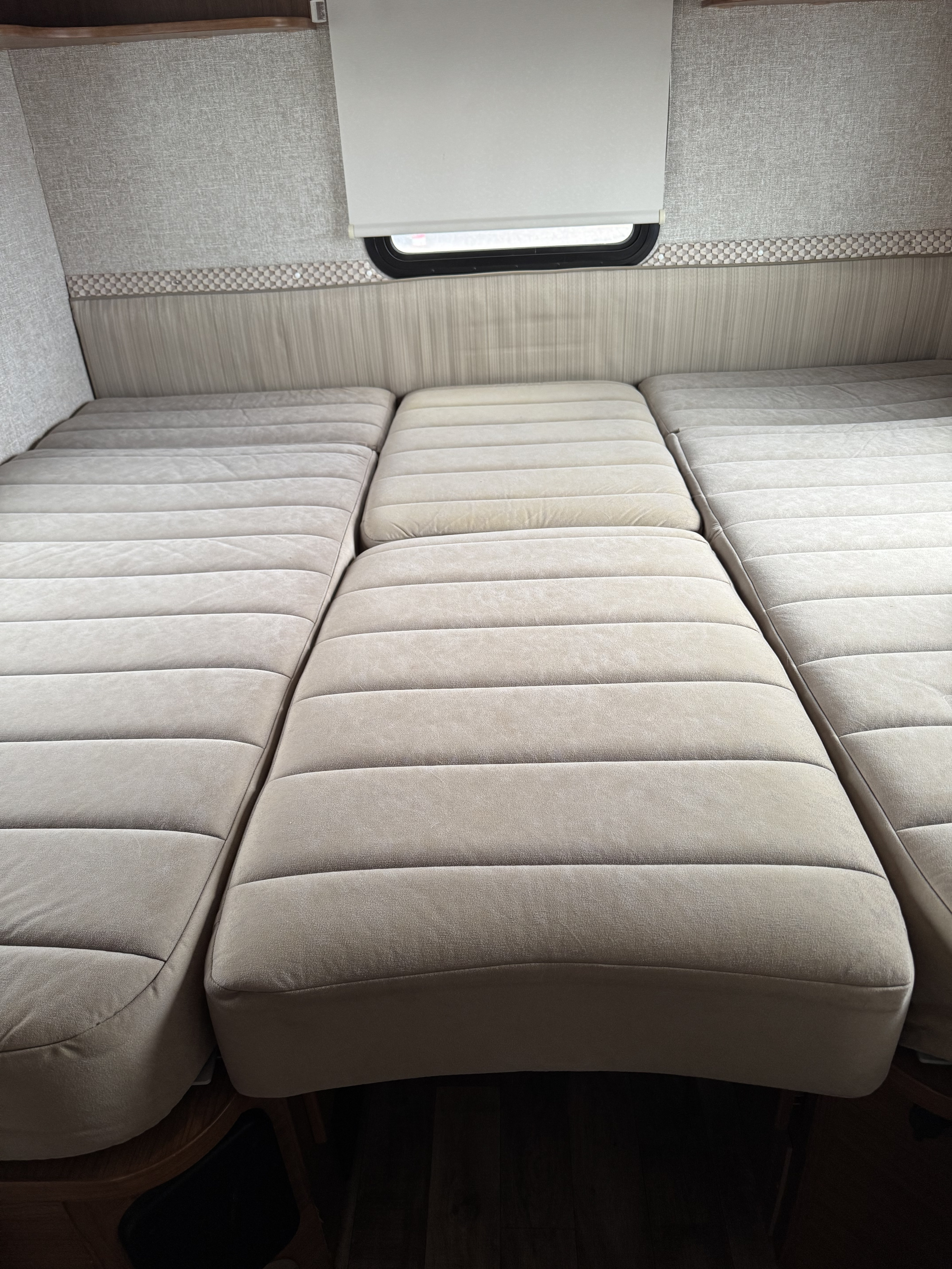 Cozy RV rental interior: three light-colored, padded cushions forming a bed below a window with a shade.. Winnebago View 2017