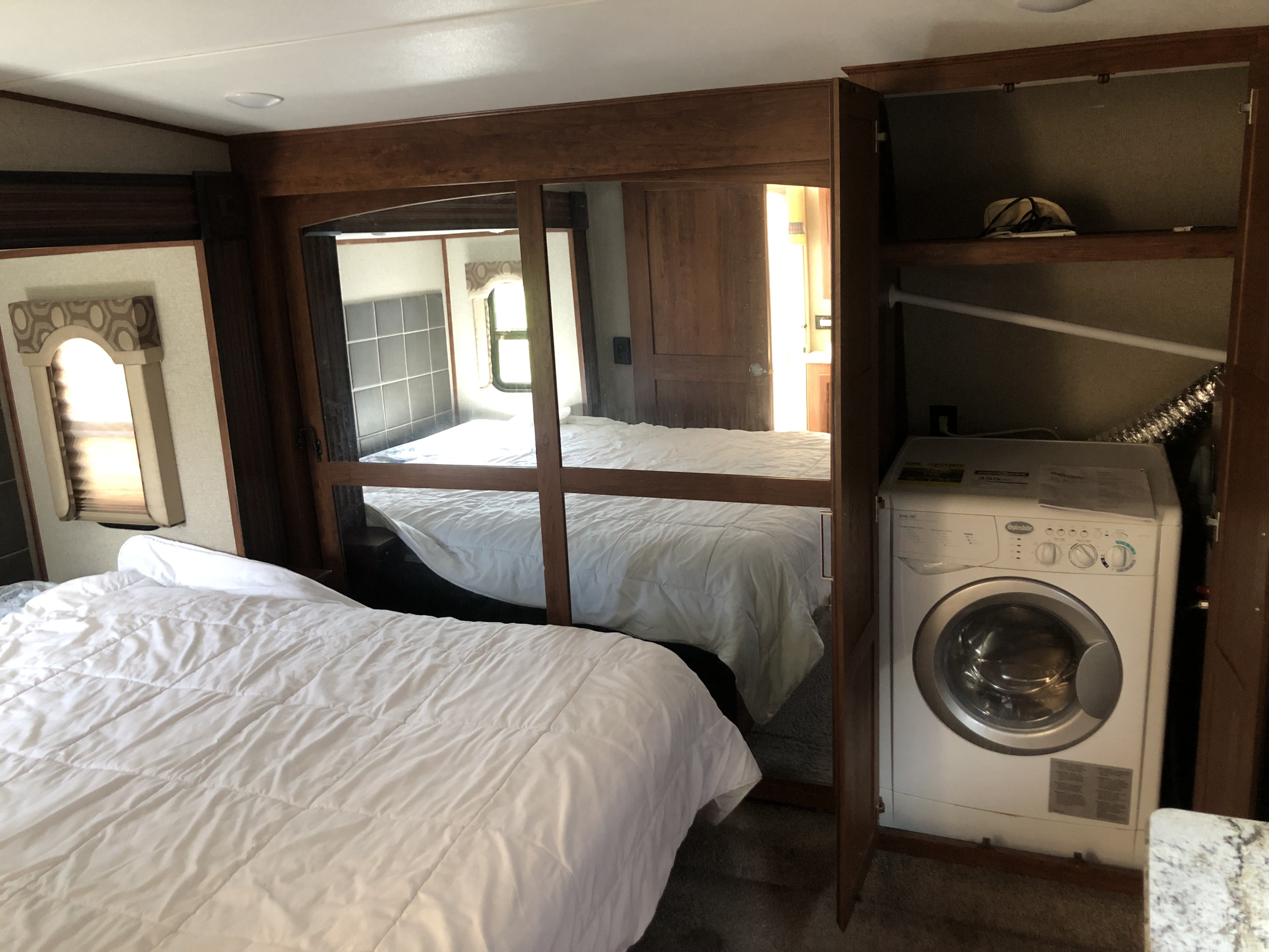 RV rental bedroom showcasing a bed, mirrored wardrobe, and a compact washer/dryer unit for convenience.. Keystone RV Avalanche 2017