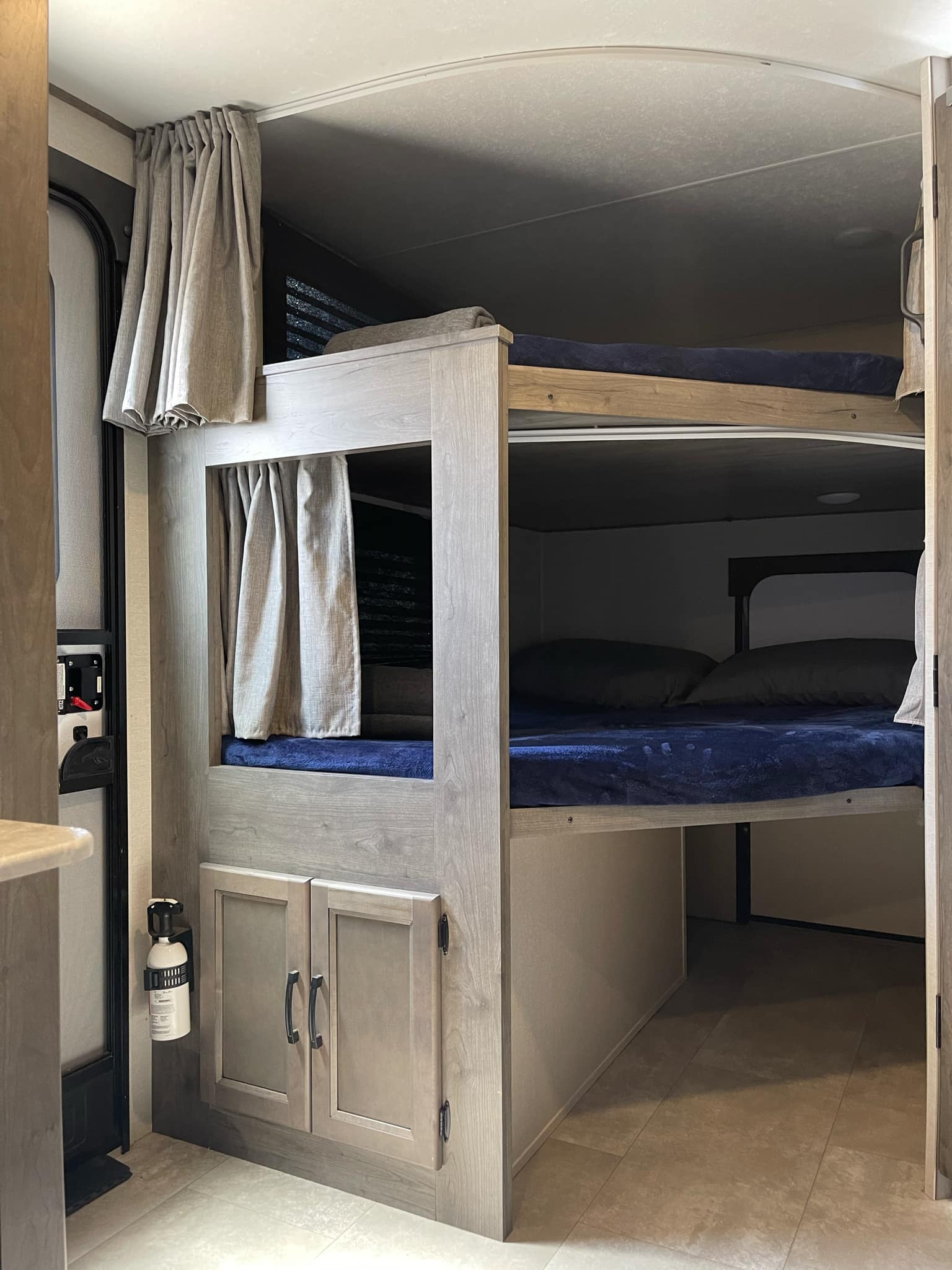 Cozy bunk beds with privacy curtains and storage built into this RV rental interior, complete with a mounted fire extinguisher.. Coachmen Apex 2021