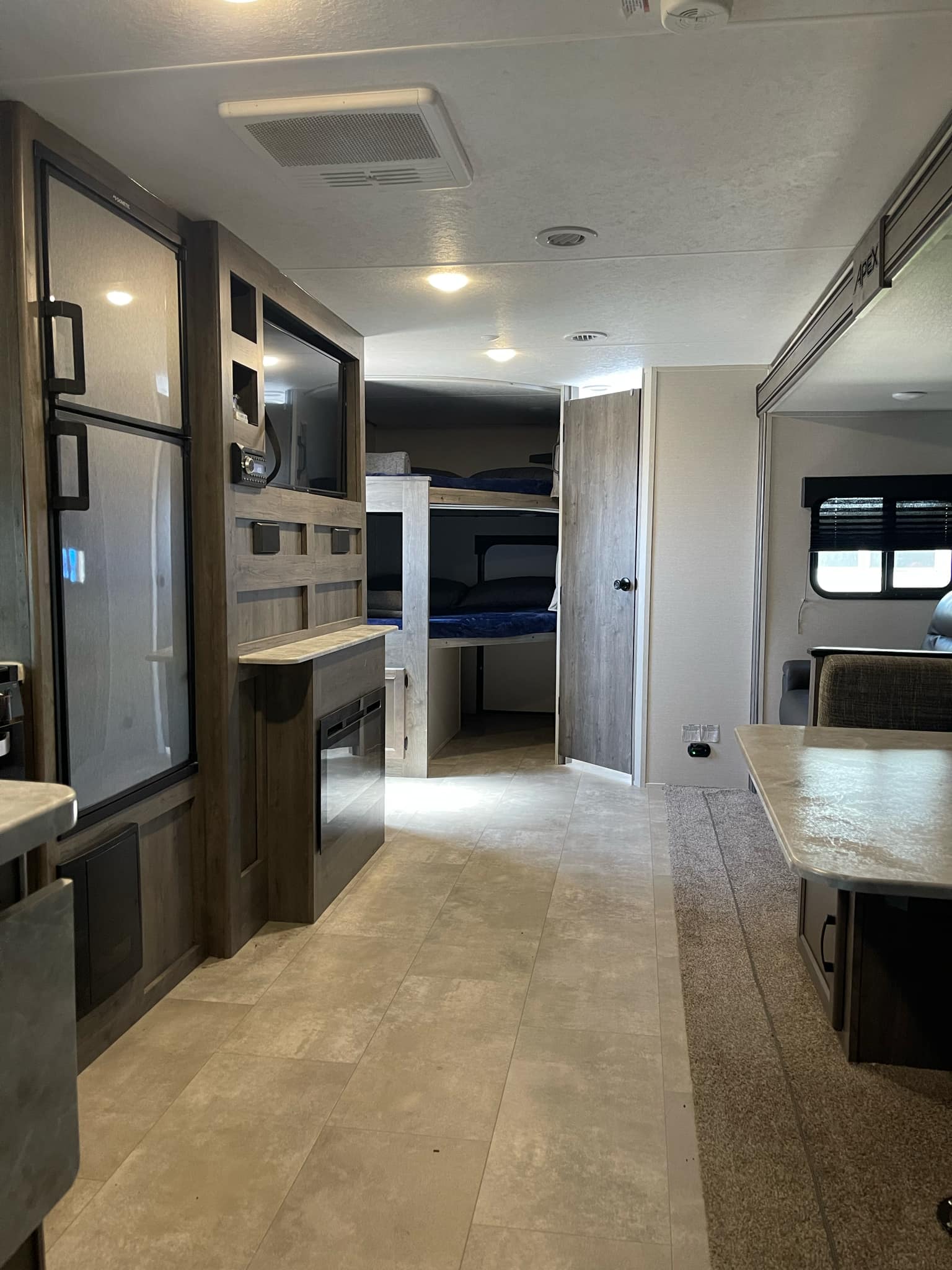 Interior of an inviting rv rental. Features modern kitchen, entertainment center with fireplace, bunk beds, and dining space.. Coachmen Apex 2021