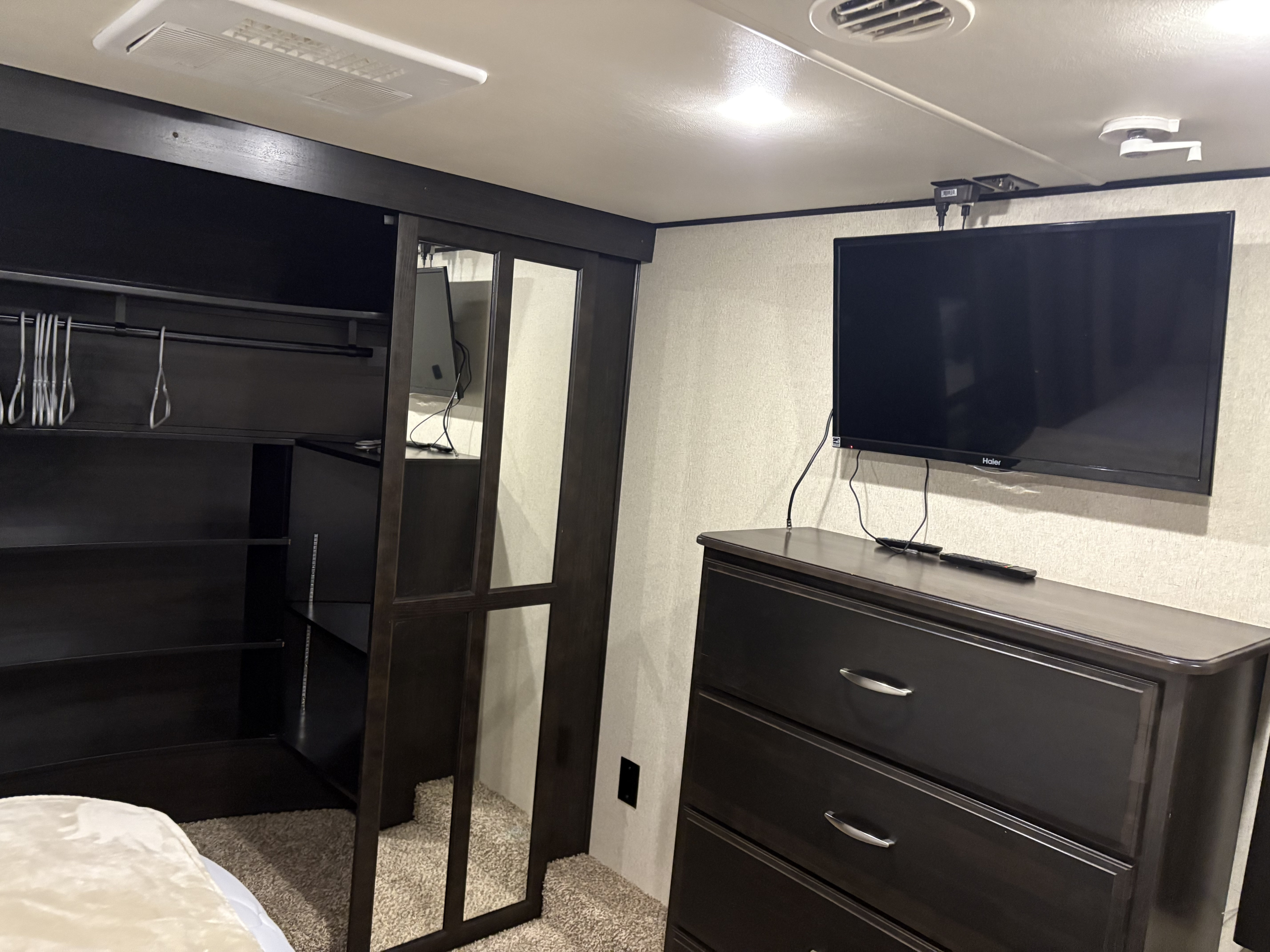 A cozy RV rental interior showcasing a dark wood closet with mirrored doors, shelves, and a dresser with a TV.. Grand Design Momentum Toy Hauler 2015