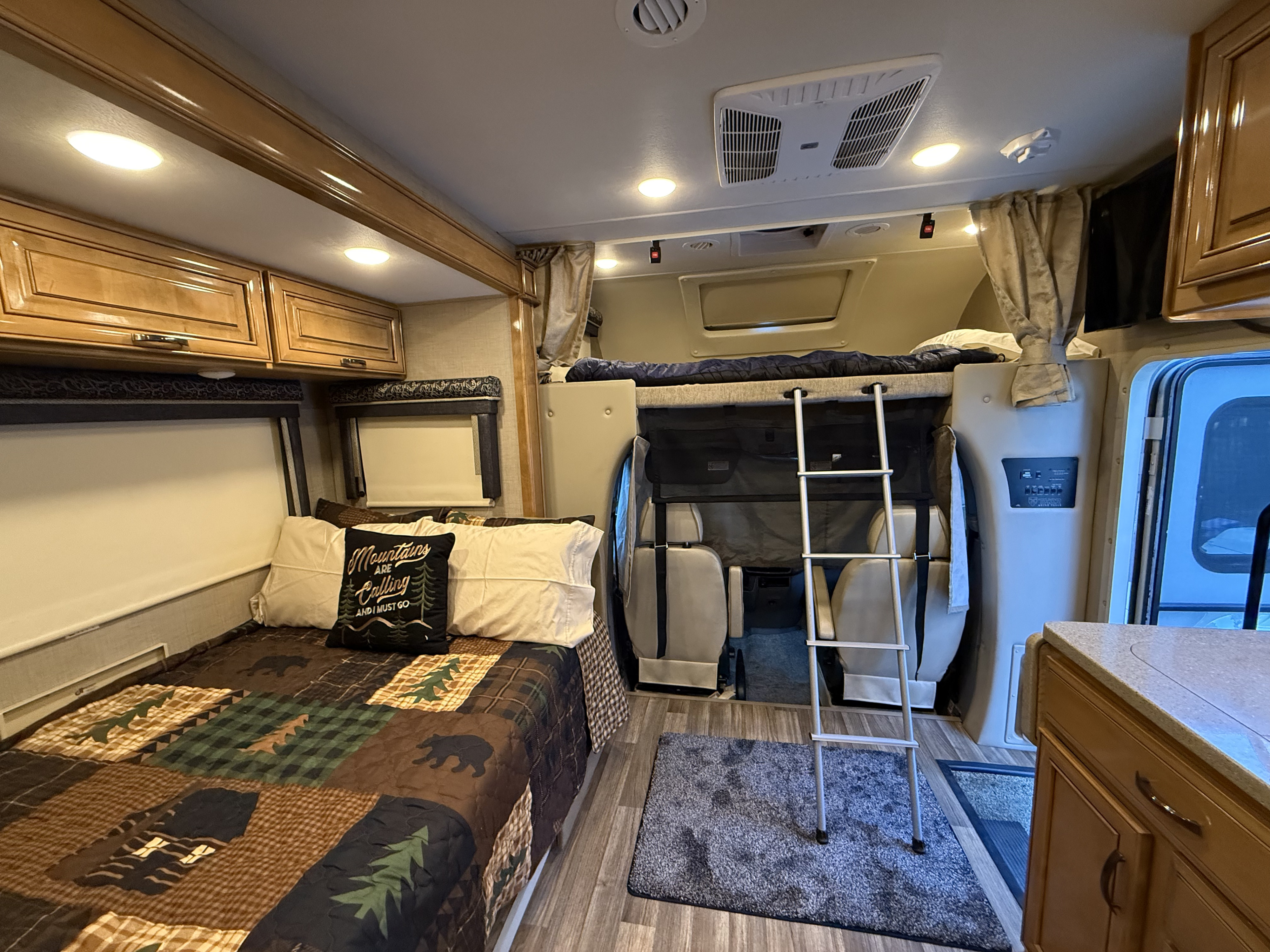 Spacious RV rental interior with bedroom, overhead bunk, kitchen counter, and cockpit area visible.. Thor Quantum 2018
