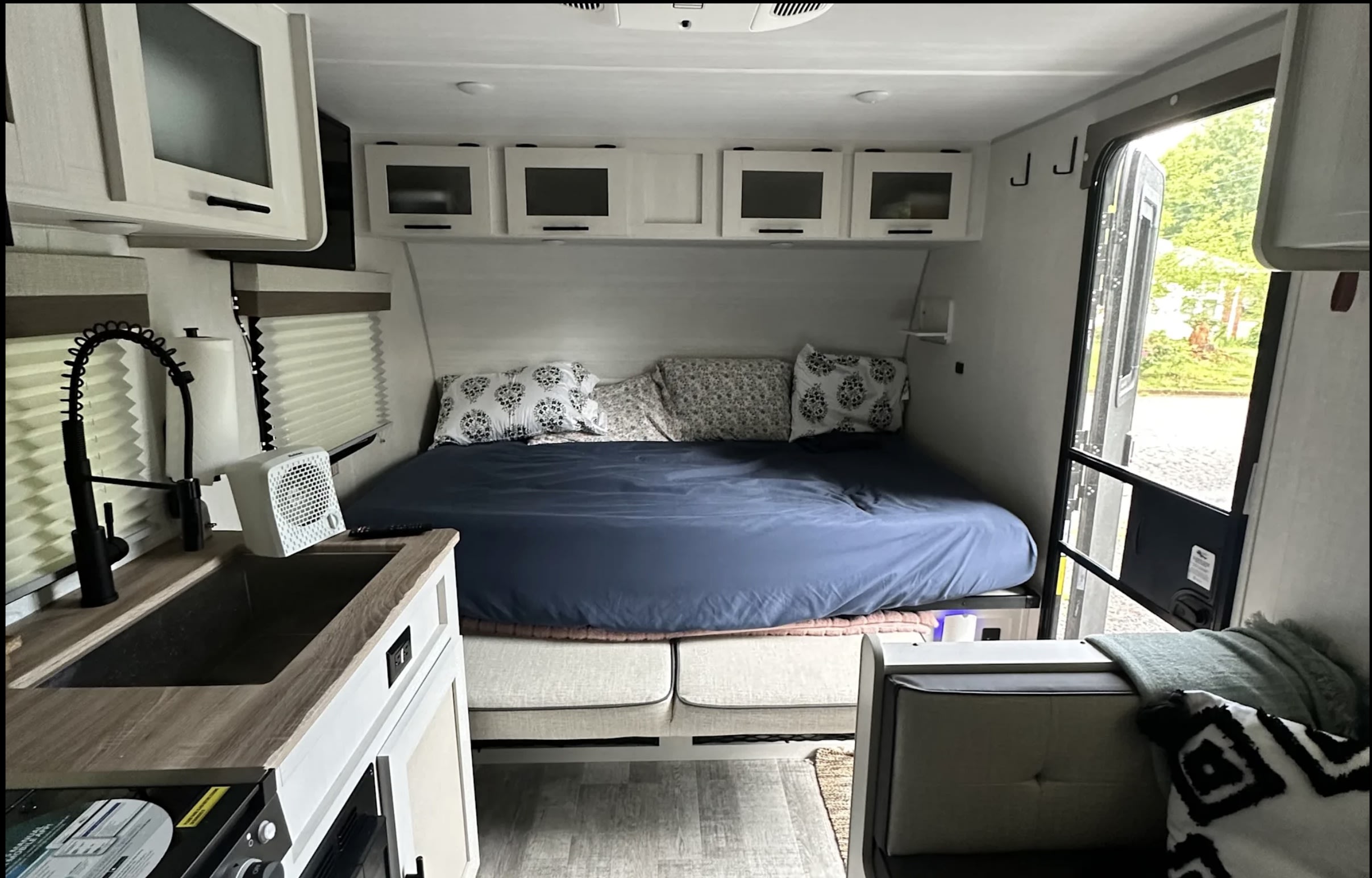 Cozy RV rental interior: bed, compact kitchen with sink, and open door. Perfect for travel adventures on the road.. Forest River No Bounderies 2024