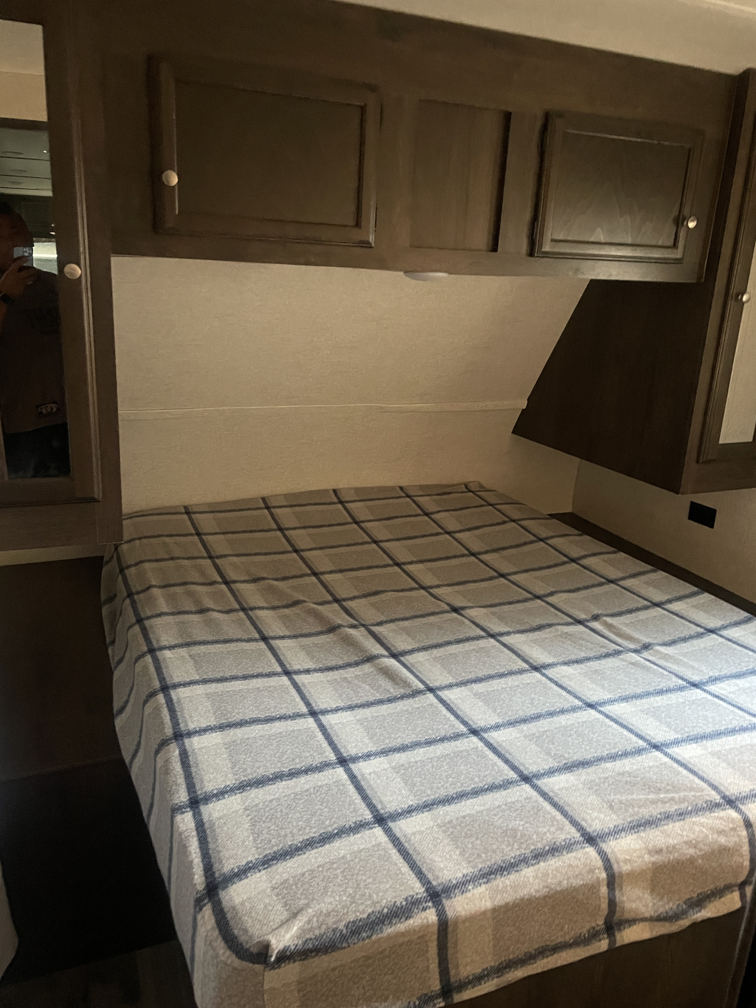 Inside an RV rental: a comfortable bedroom with a plaid bedspread, dark wood cabinets, and a reflective mirrored closet.. Jayco 262 2018