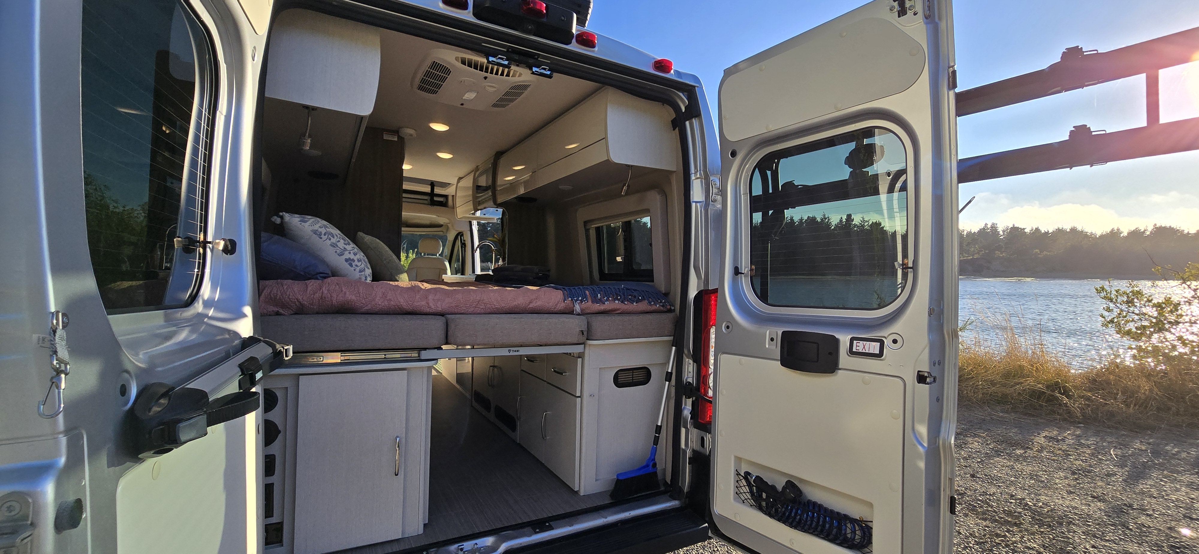 RV rental camper van interior with comfy bed opens to stunning waterfront nature view.. Thor Tellaro 2024
