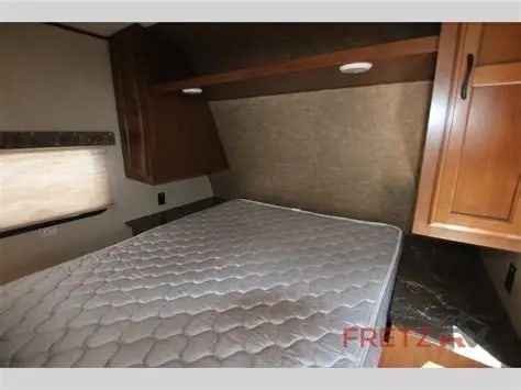 RV rental interior showing a cozy bedroom with a white mattress, overhead wood cabinets, and a window.. Jayco Jay Flight SLX 2016