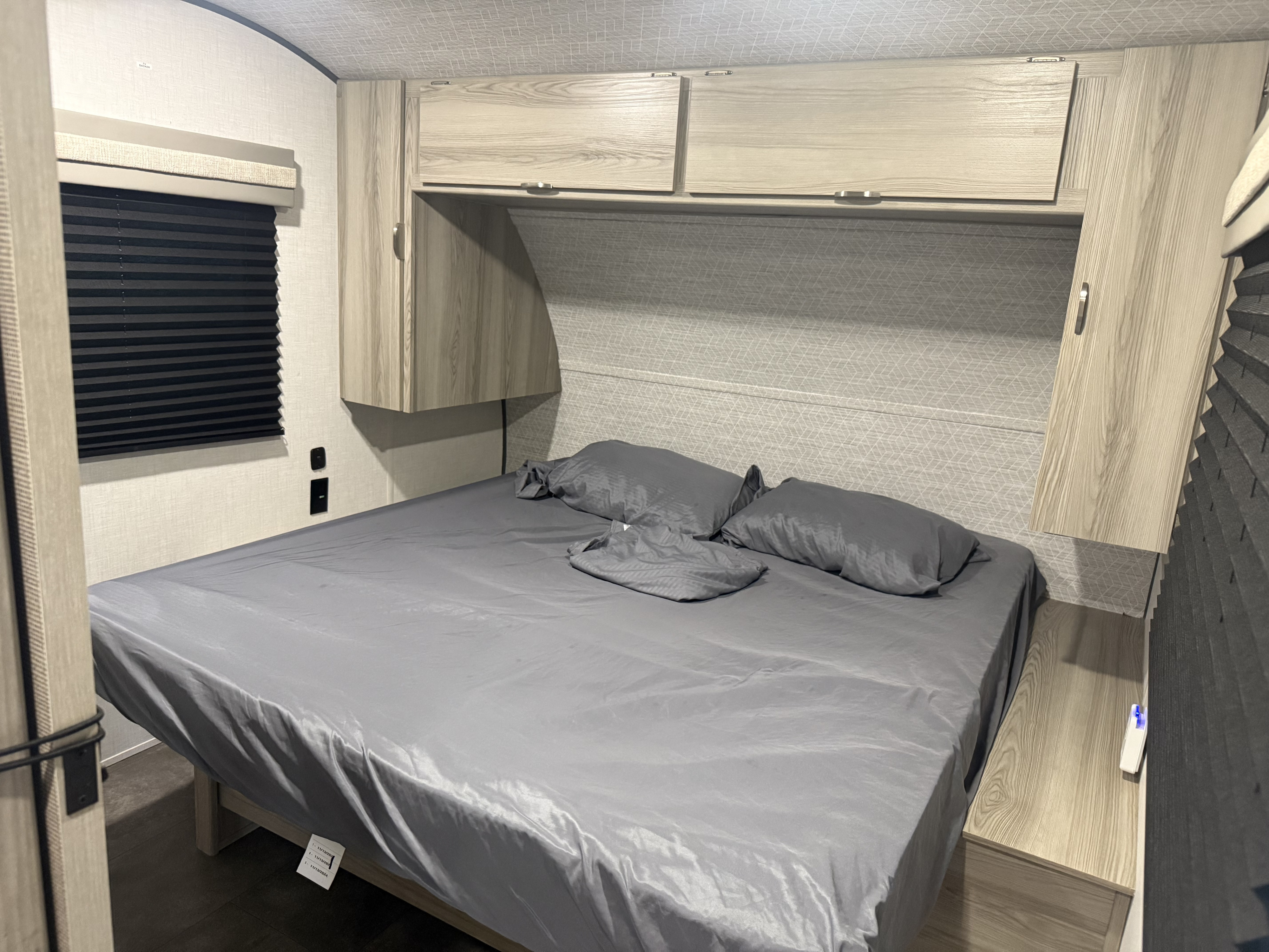 Spacious bedroom in an RV rental, featuring a large bed with grey bedding, overhead cabinets, and a window for comfortable stays.. Forest River Salem fsx 266bhle 2025