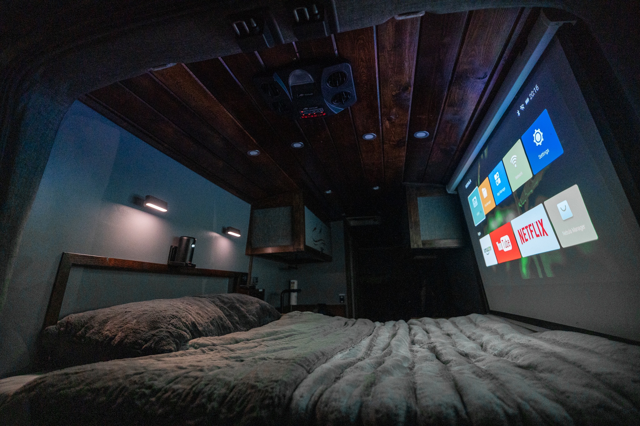 Cozy RV rental bedroom features a ceiling projector beaming entertainment onto a screen for ultimate comfort.. Ford Transit 350 HD XL 2020