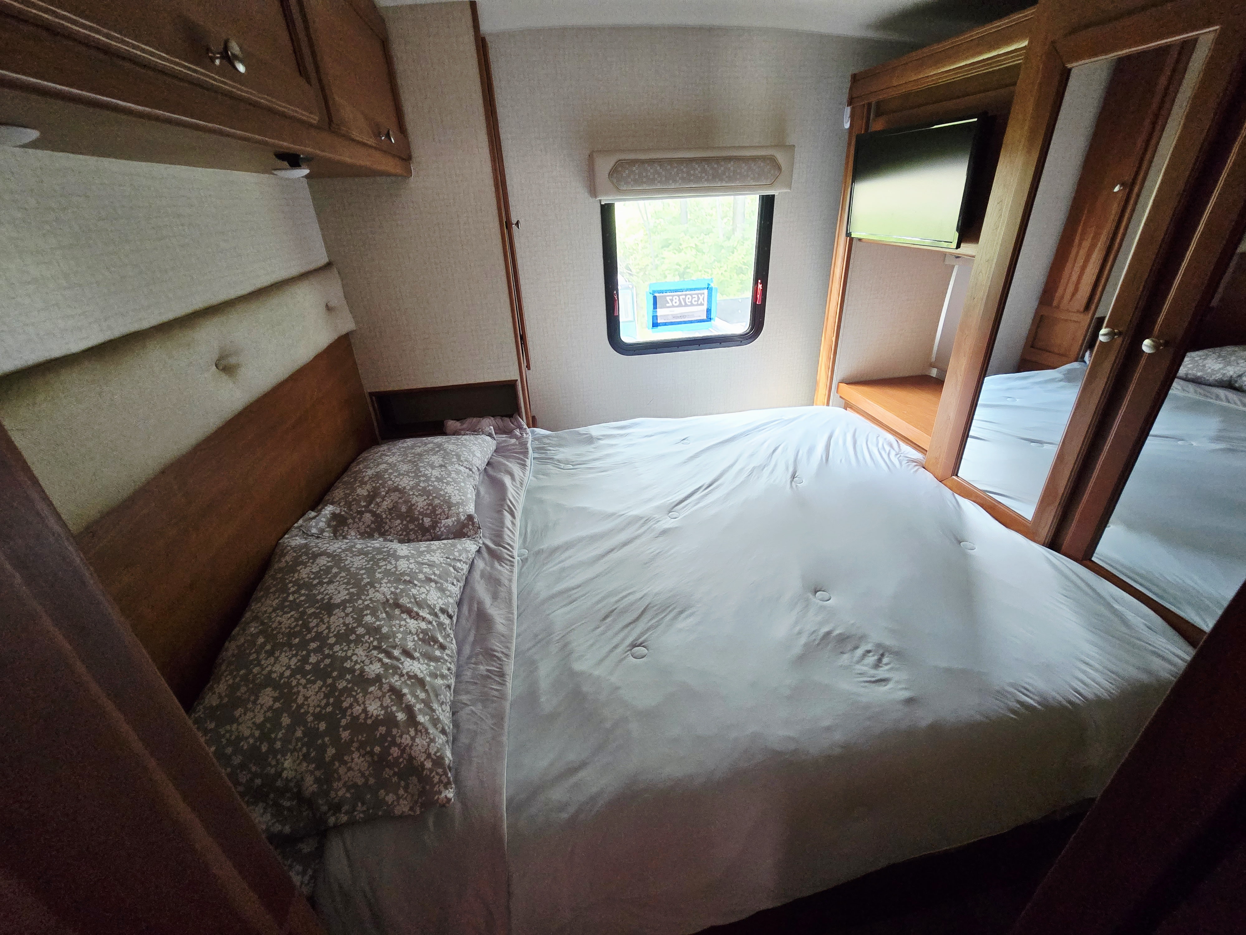 A clean, inviting bedroom with a made bed inside an RV rental. Features a window and mirrored closet.. Winnebago Vista 2017