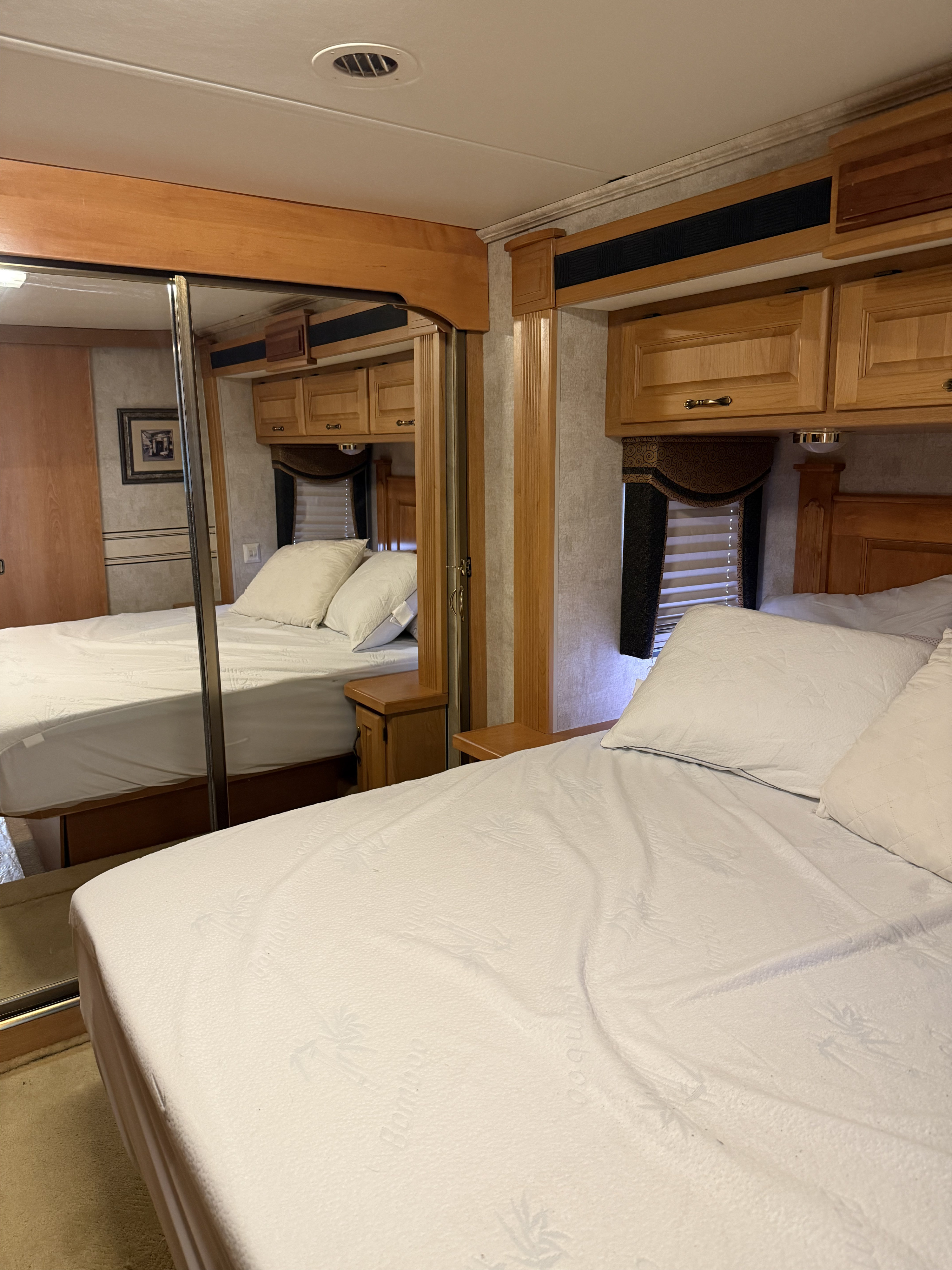 Inside an RV rental: a bright bedroom with mirrored closet, wooden cabinets, and a comfortable bed featuring bamboo-themed bedding.. Monaco Knight 2006