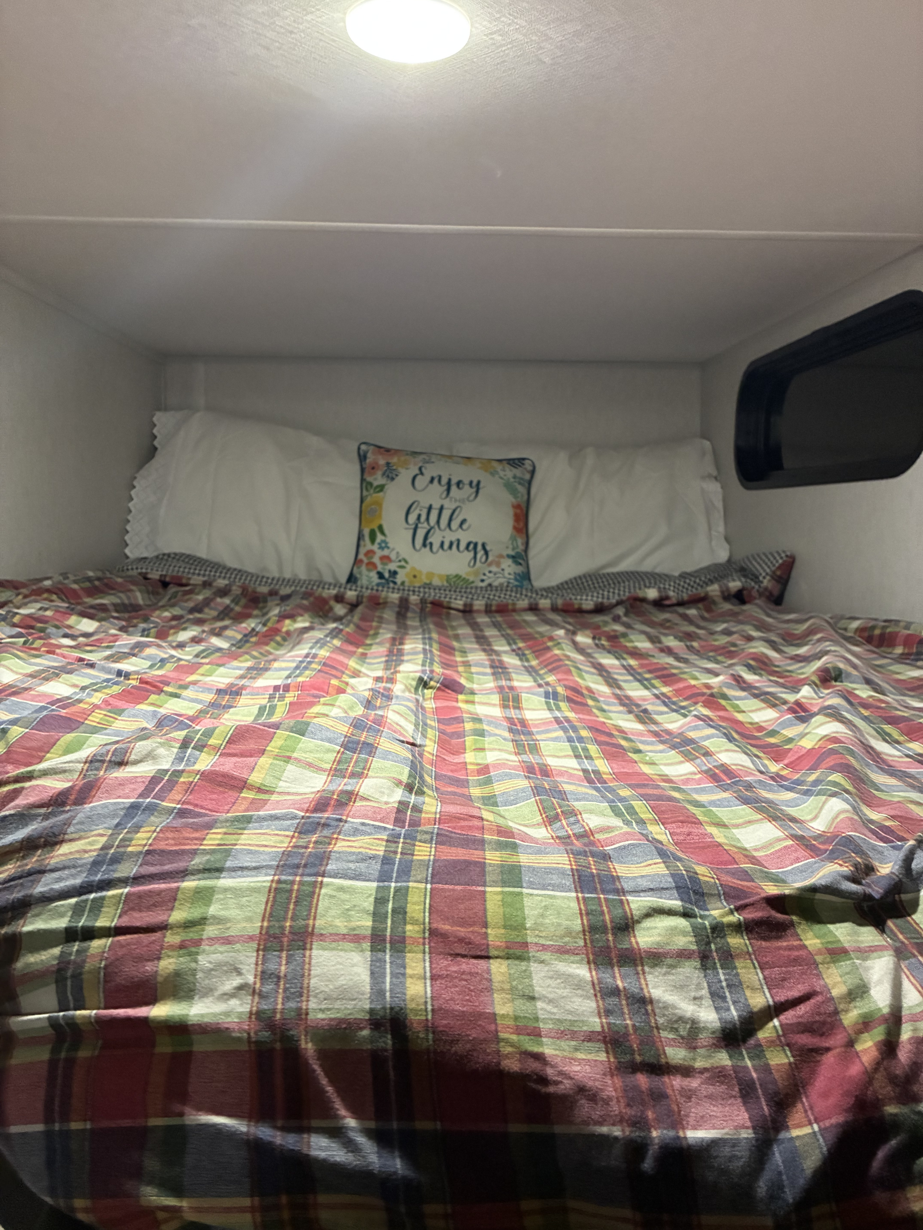 Inside an RV rental: a cozy bunk bed with colorful plaid bedding, white pillows, and a cheerful "Enjoy little things" pillow.. Forest River Cherokee Grey Wolf 2024