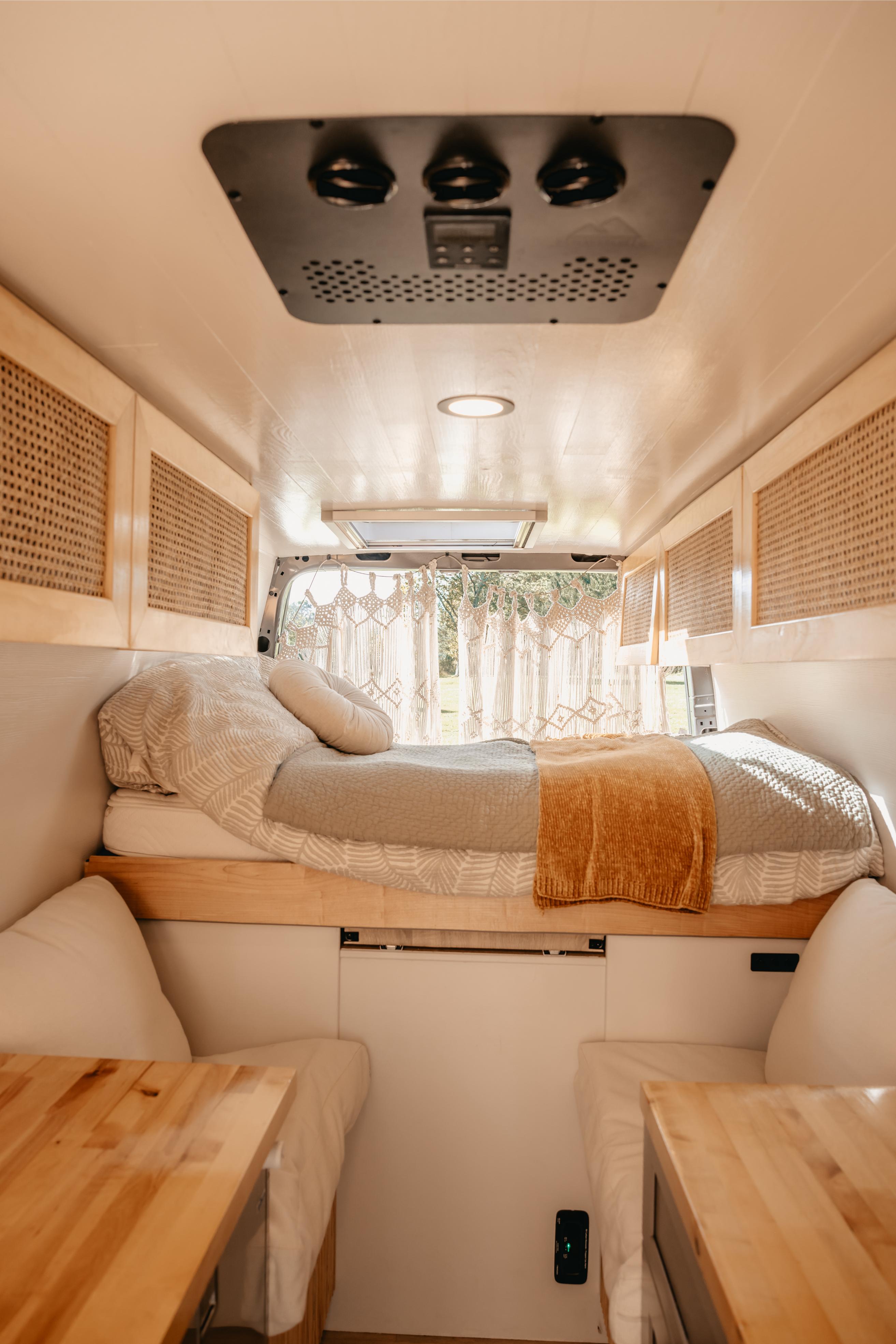 Explore this cozy RV rental camper van interior featuring a bed, overhead storage, tables, and roof fan.. Mercedes-Benz Sprinter 2022