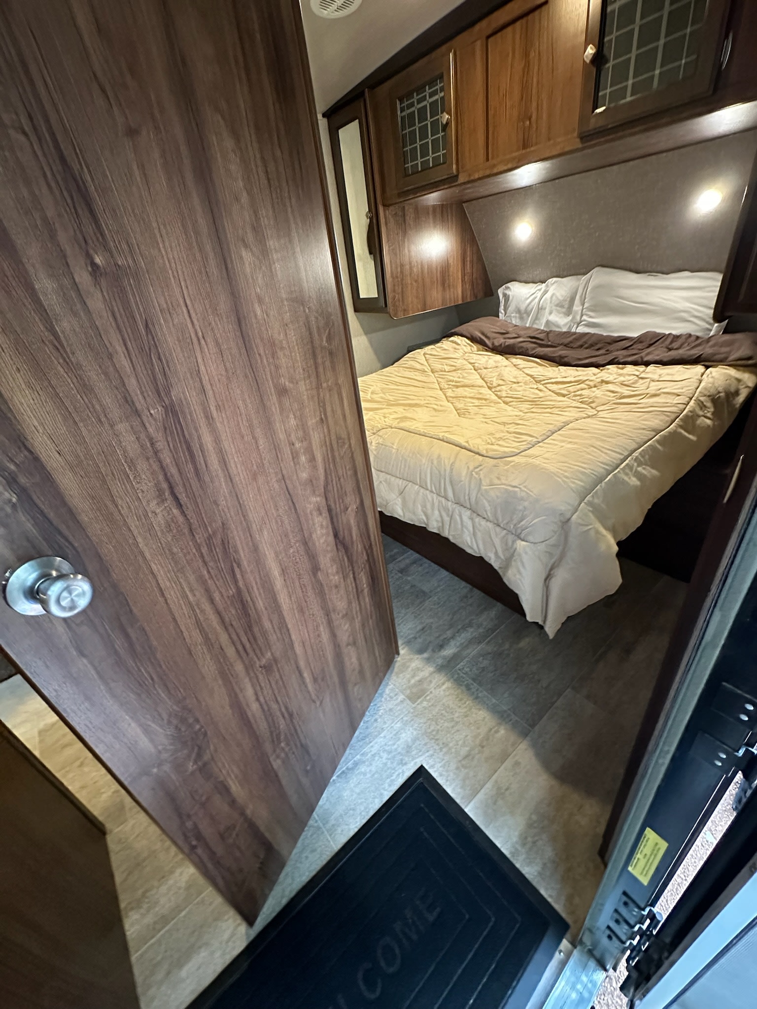 RV rental bedroom features a comfy bed, overhead cabinets, and warm lighting, perfect for your travels.. Heartland RVs Mallard 2019