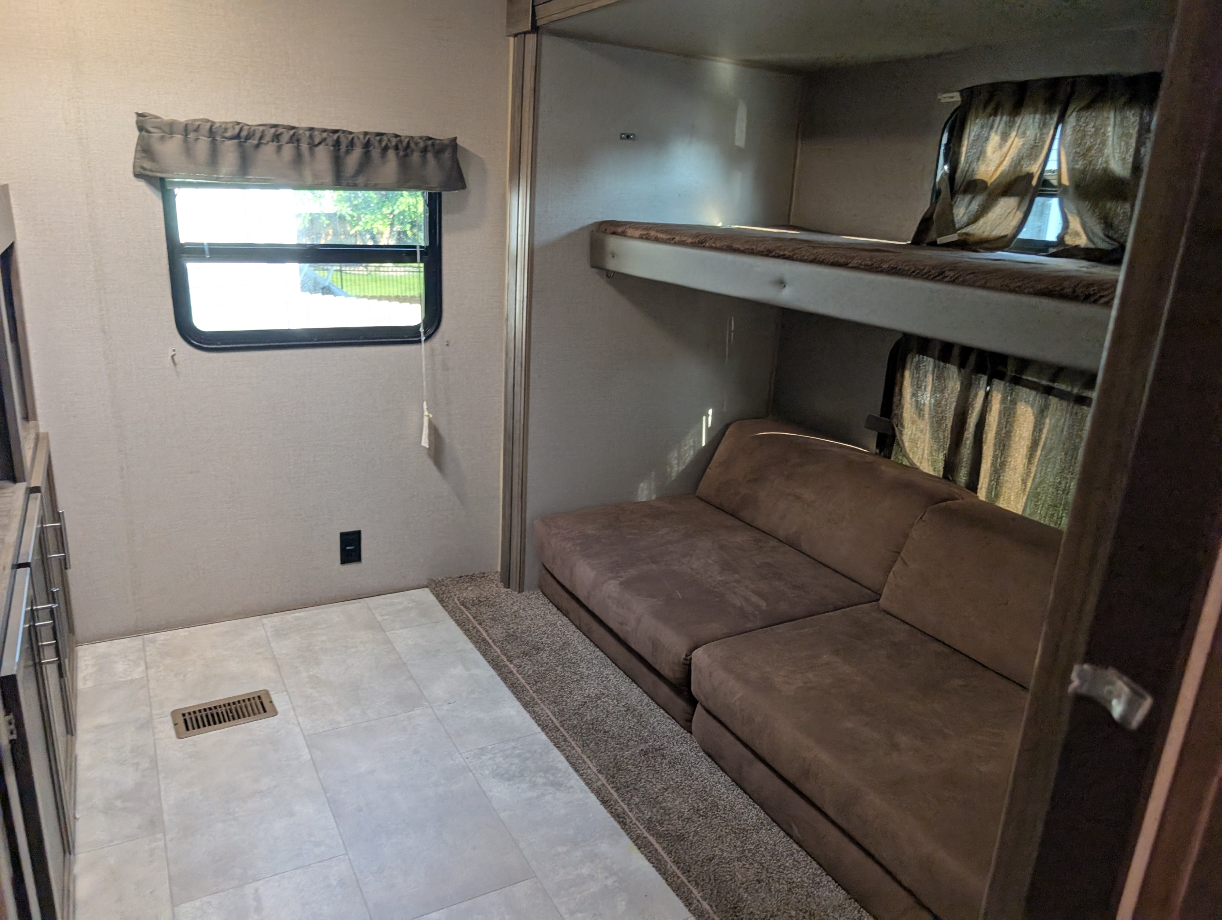 RV rental interior: practical bunk beds, a brown sofa, and window views define this comfortable living space.. Forest River Coachmen Aurora 2022