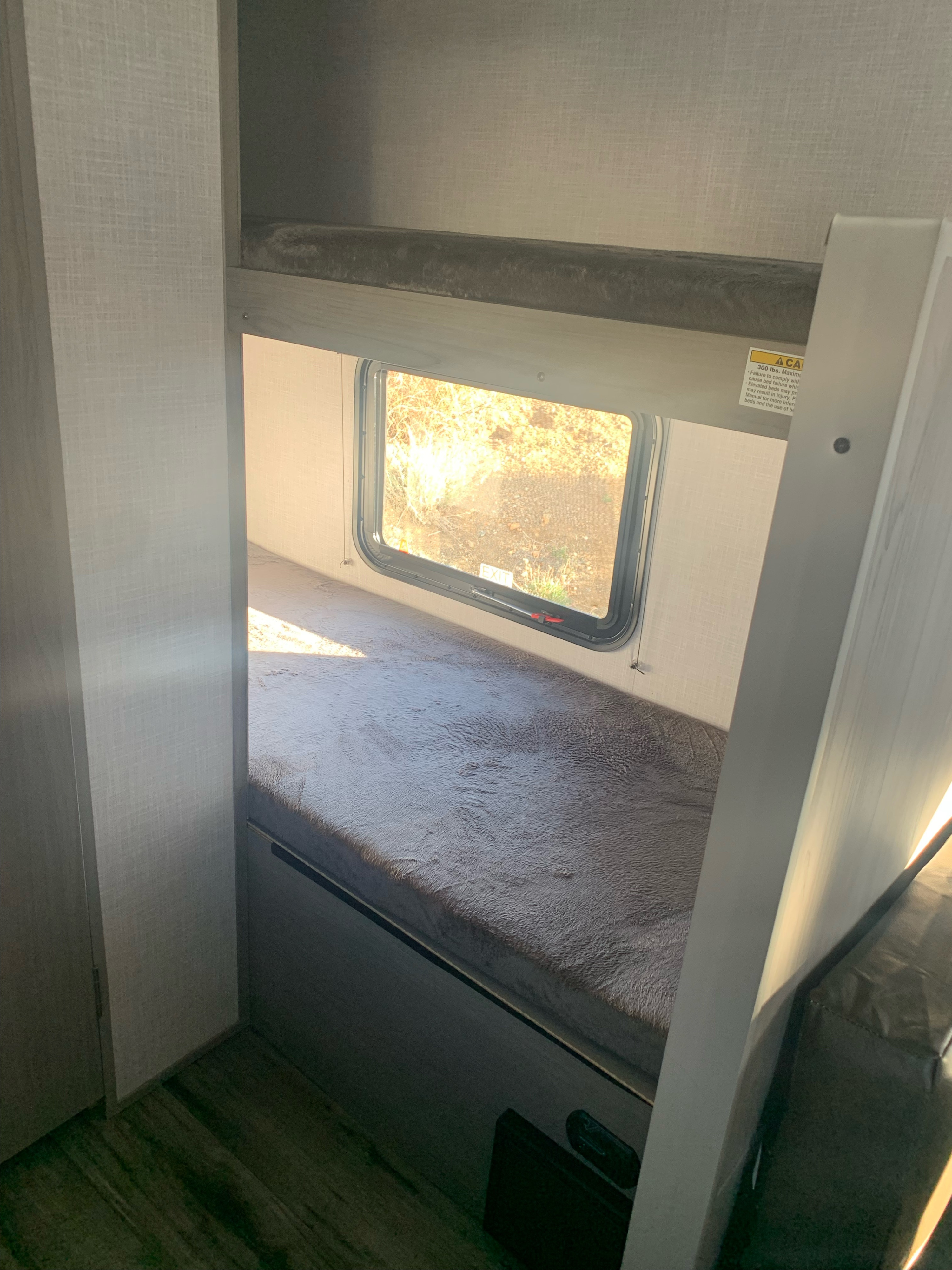 RV rental interior: cozy bunk beds with soft bedding, window view, and safety info. Ideal for travel.. Dutchmen Coleman Lantern LT 2022