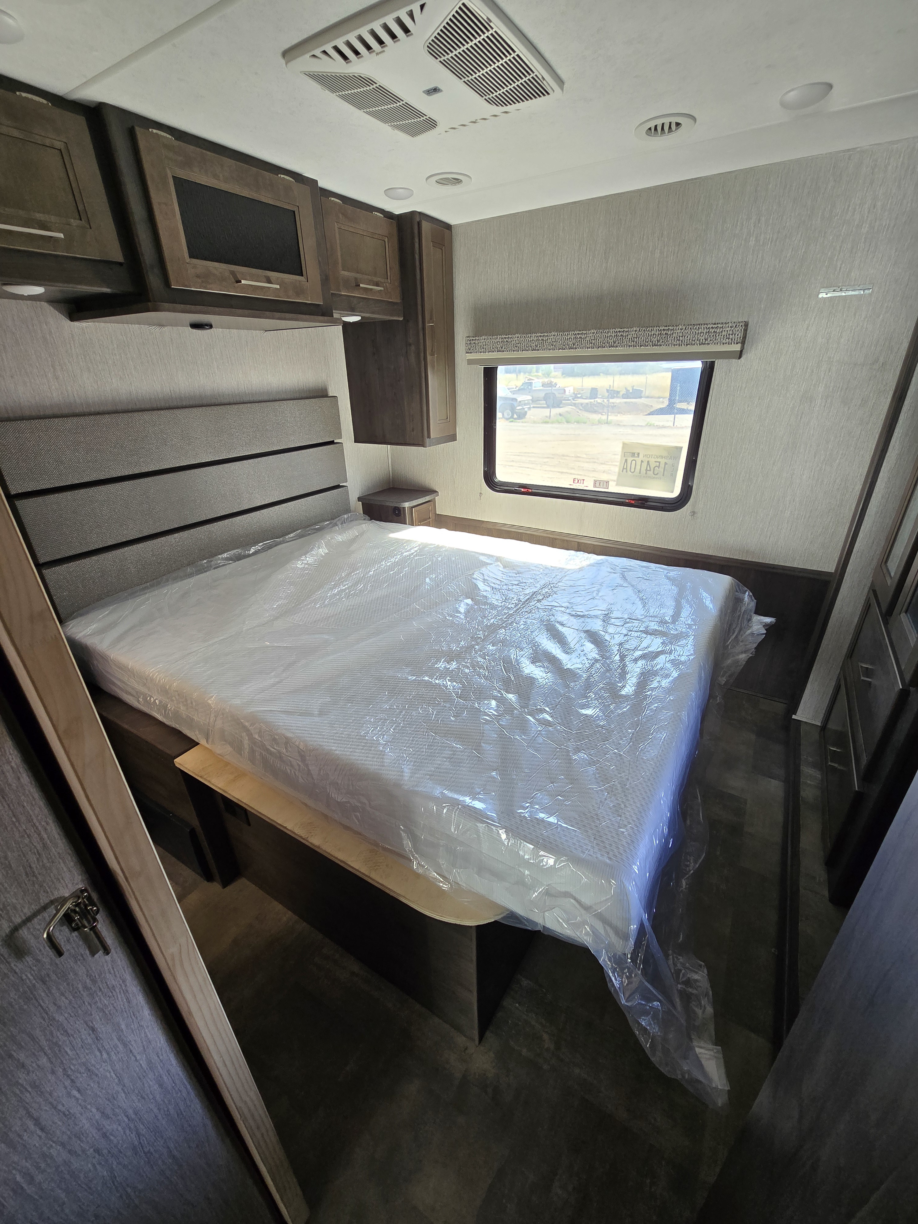 Spacious RV rental bedroom featuring a new queen bed with wrapped mattress, overhead storage, and window with outdoor view.. Forest River Coachmen Pursuit 2021